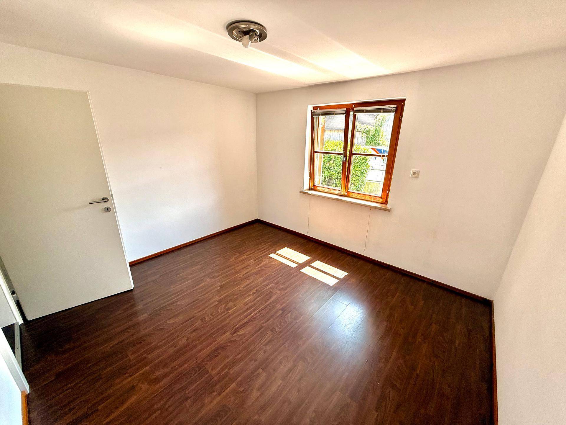 Helles Schlafzimmer mit dunklem Laminatboden und weiß gestrichenen Wänden, bereit zur individuellen Gestaltung.