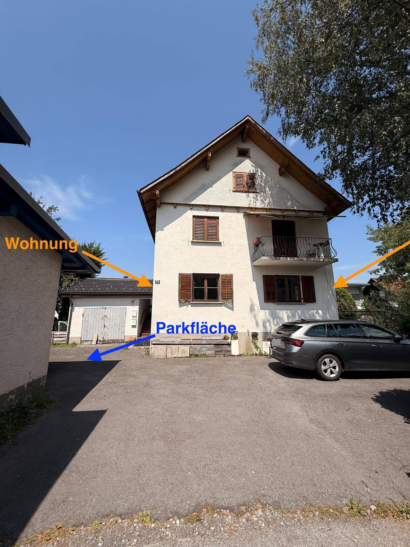 Gesamtansicht des Gebäudes mit Parkfläche und umliegender Bebauung unter blauem Himmel.