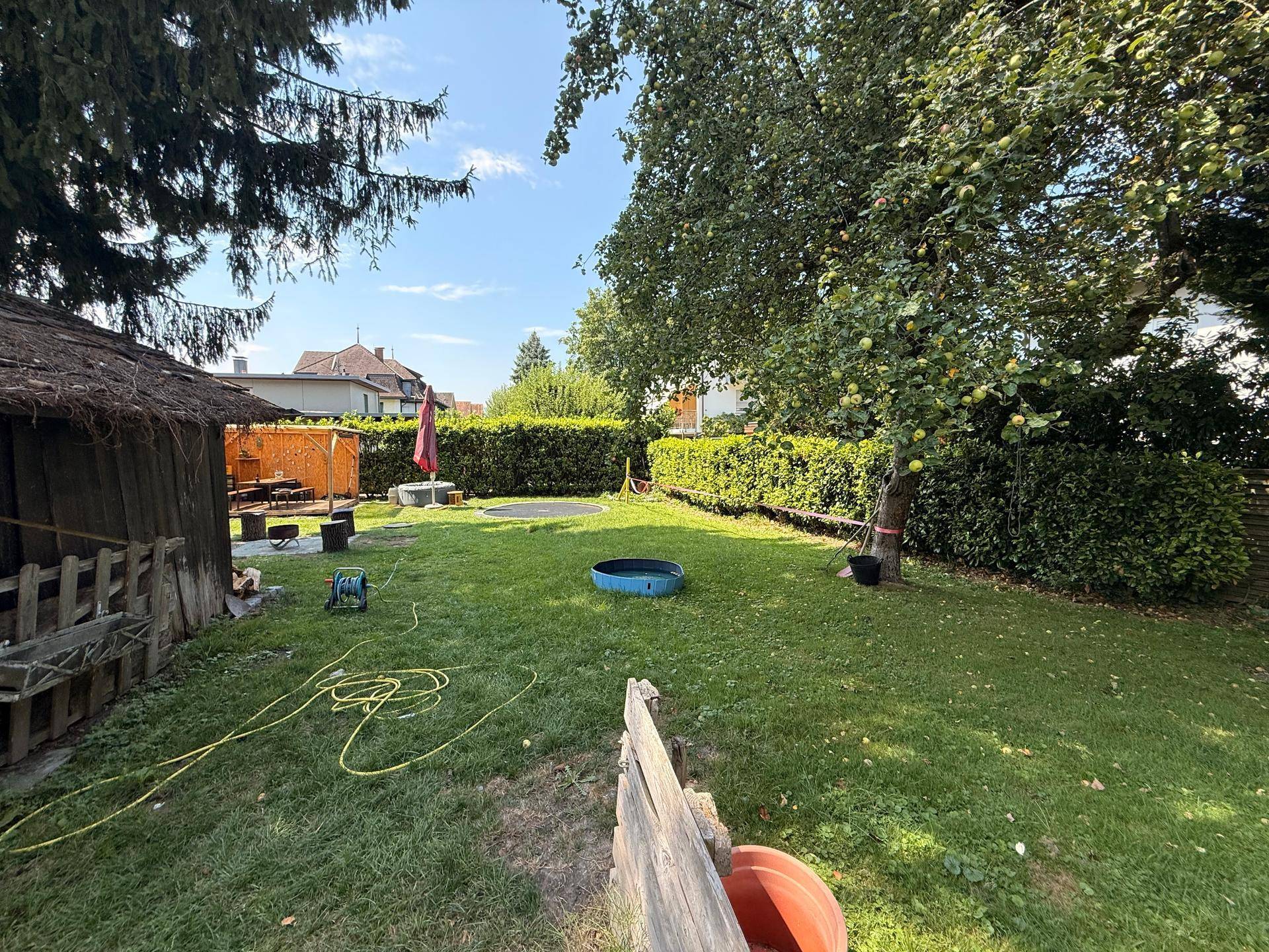Großer, gepflegter Garten mit Rasenfläche, Bäumen und einer Hecke, ideal zum Entspannen im Freien.