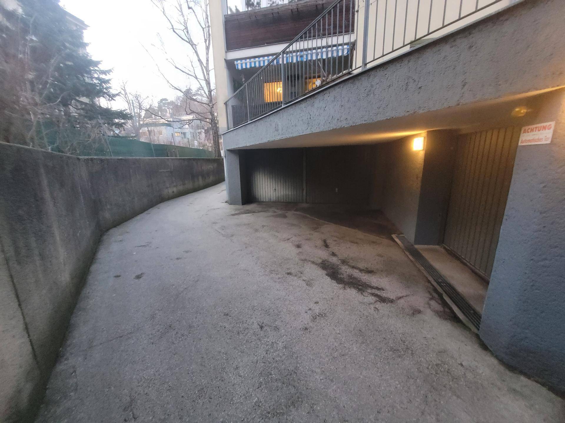 Zufahrt zur Tiefgarage mit Betonrampe und darüberliegendem Balkonbereich.