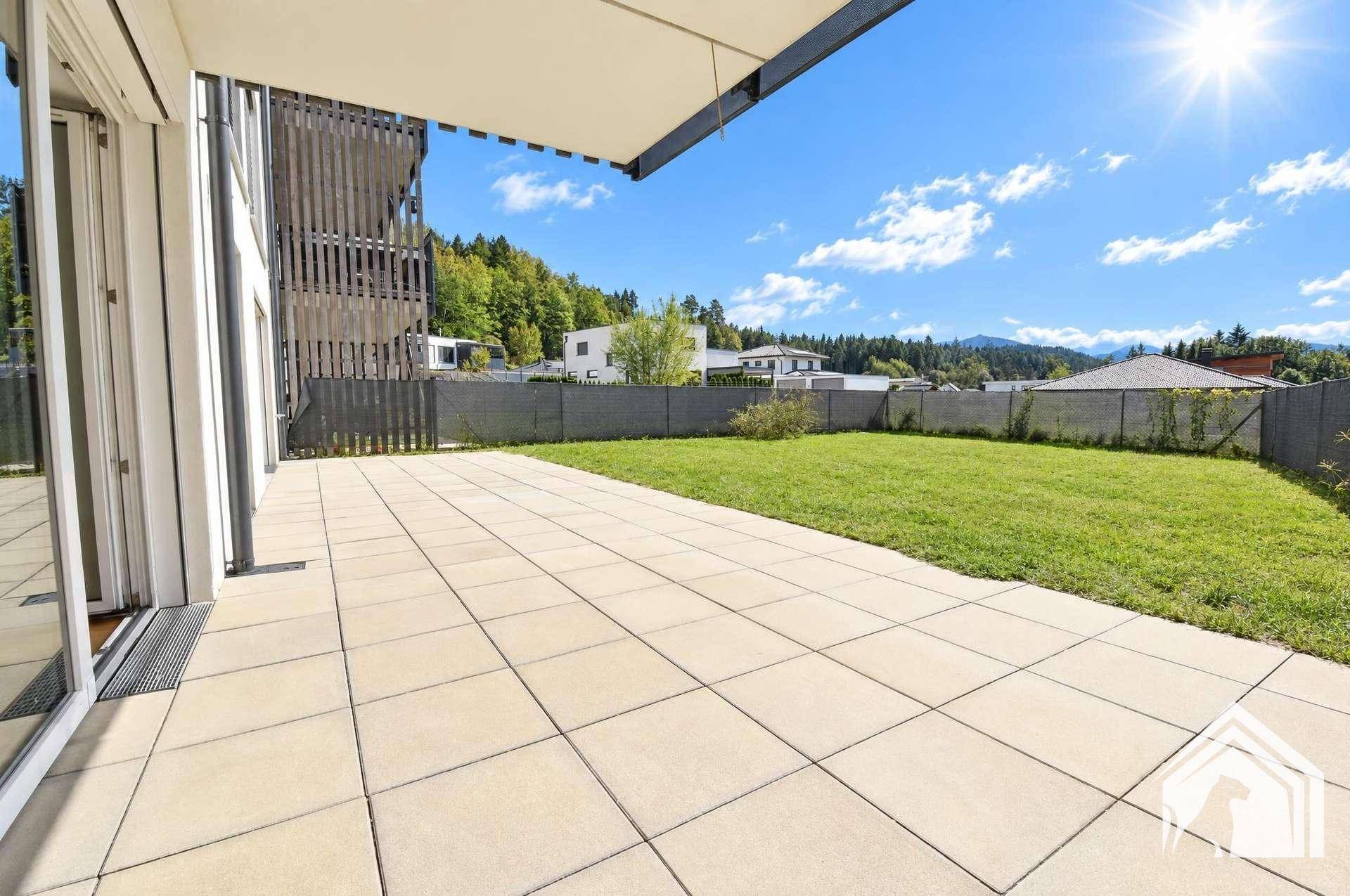 Sonniger Außenbereich mit großer gepflasterter Terrasse und angrenzender Rasenfläche.