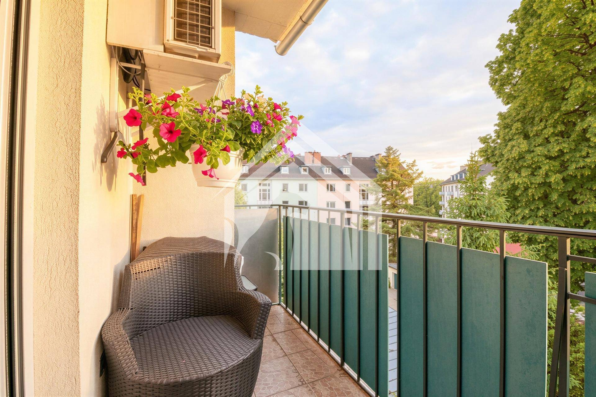 Gemütlicher Balkon mit einem Korbstuhl, Blumen und grünen Sichtschutzwänden.