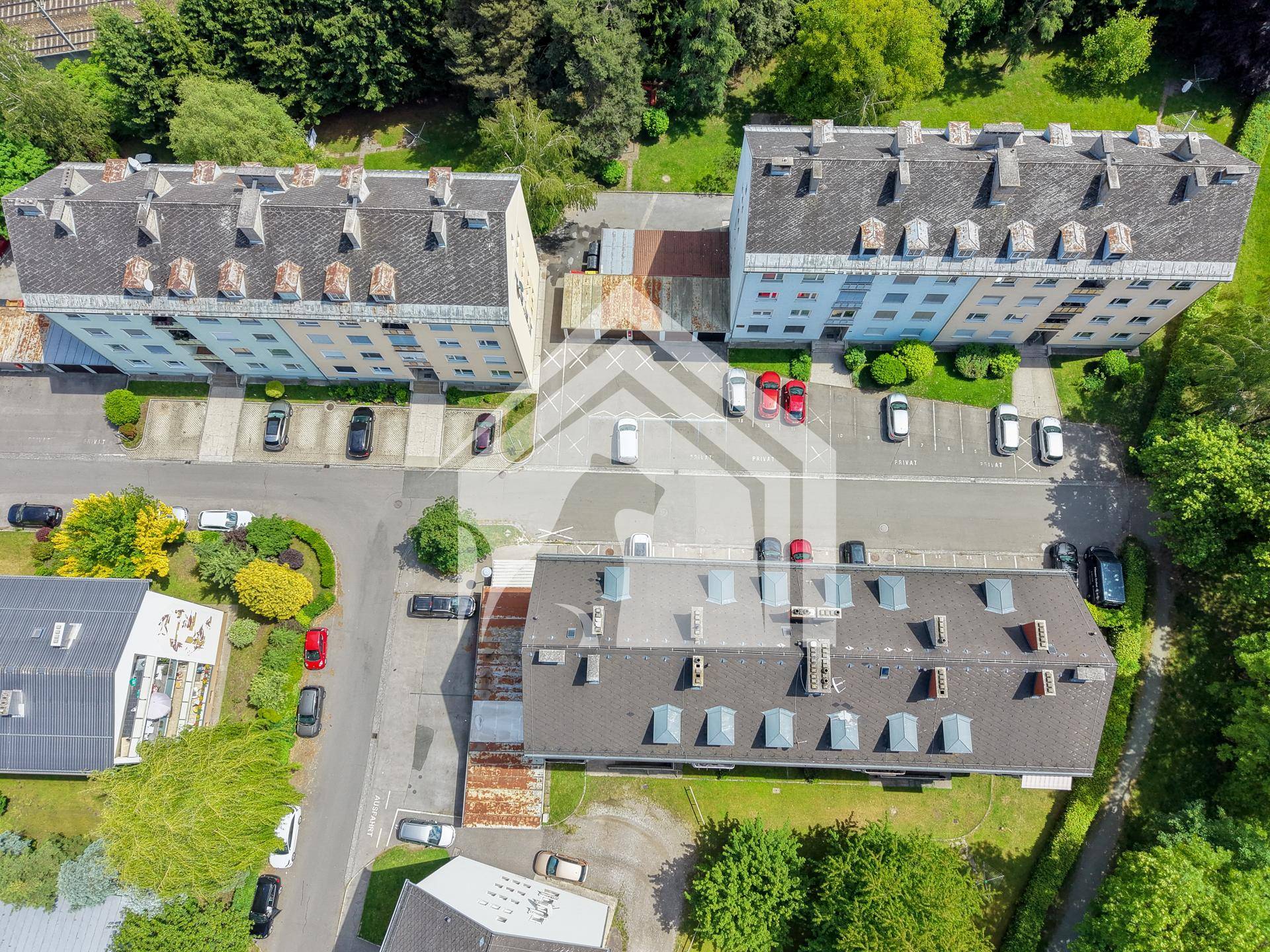 Luftaufnahme eines Wohnkomplexes mit mehreren Gebäuden und Parkplätzen im Grünen.