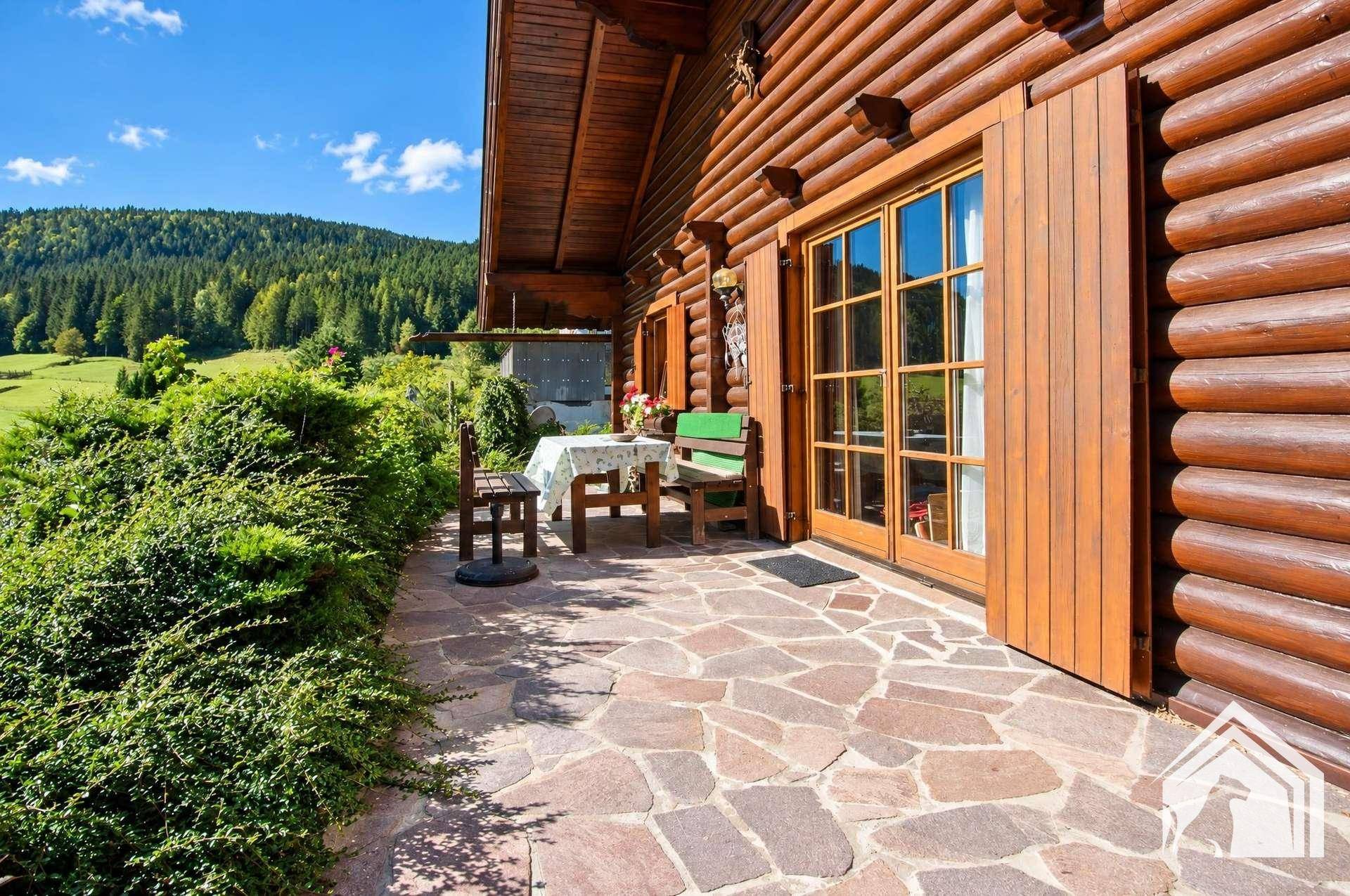 Sonnenterrasse mit Steinfliesen, Gartenmöbeln und weitem Blick auf die grüne Landschaft.