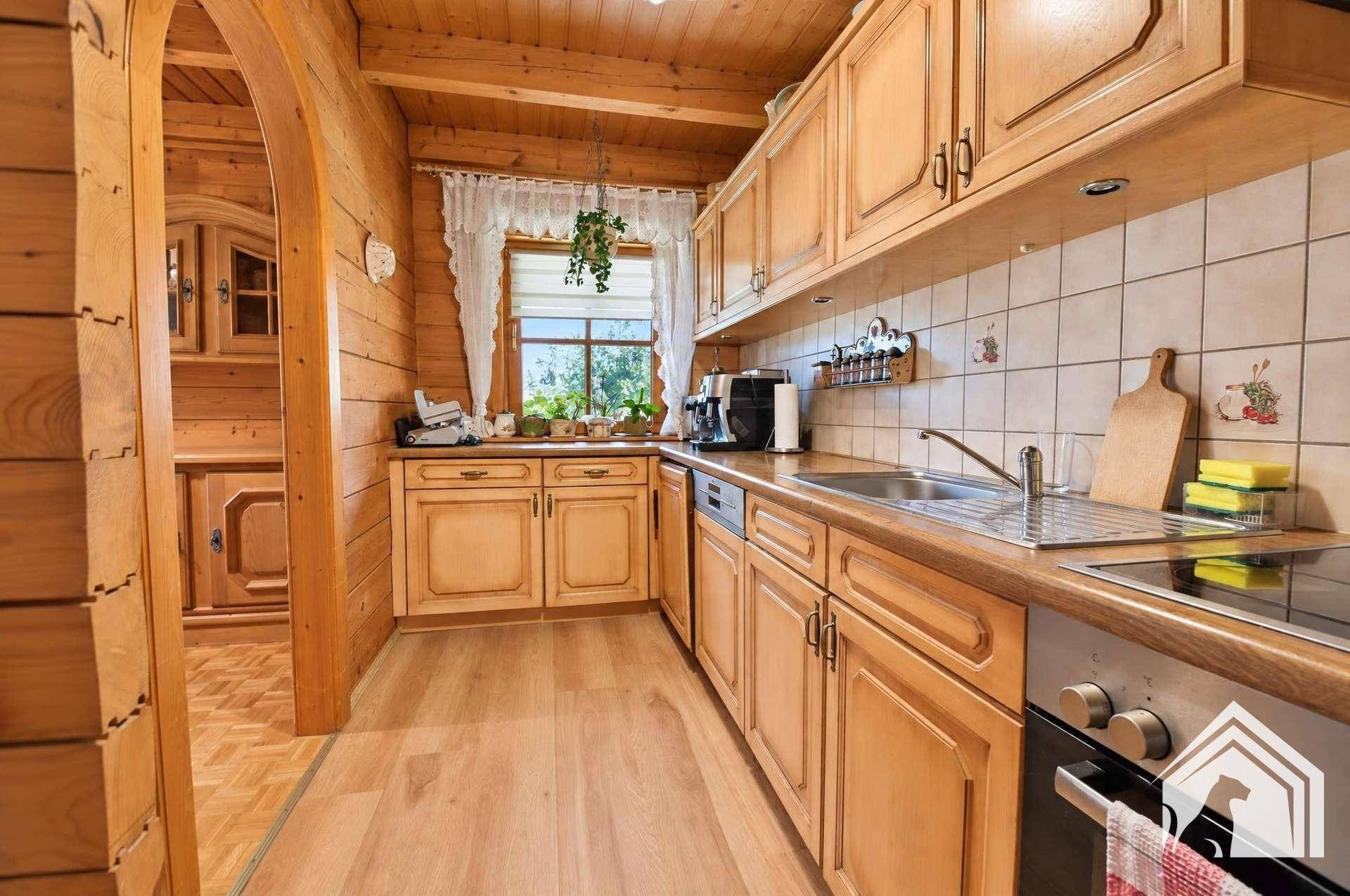 Traditionelle Holzküche mit Einbauschränken, Fliesenrückwand und Blick ins Grüne.