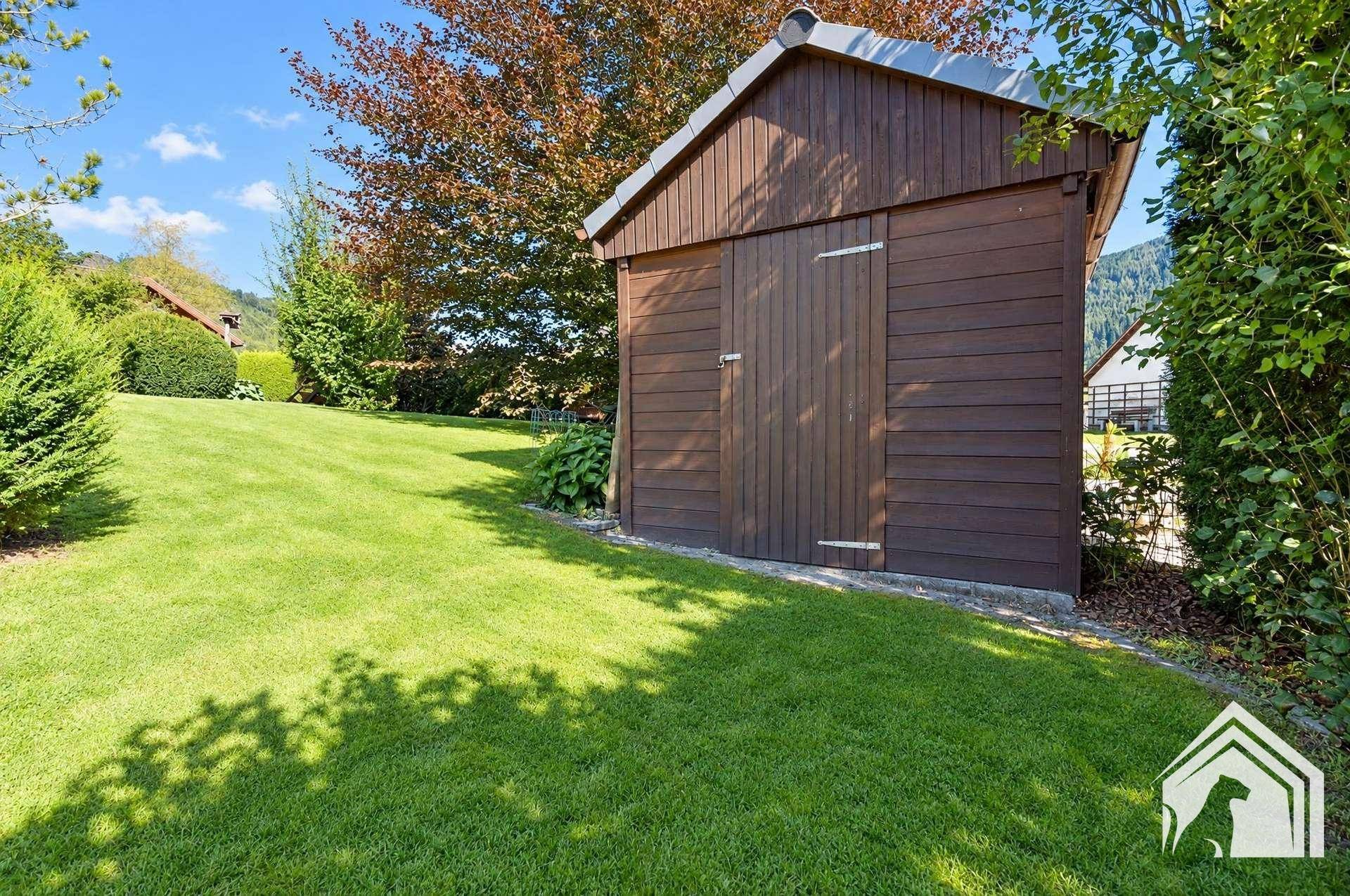 Praktischer Holzschuppen im gepflegten Gartenbereich, umgeben von Rasen und Bäumen.