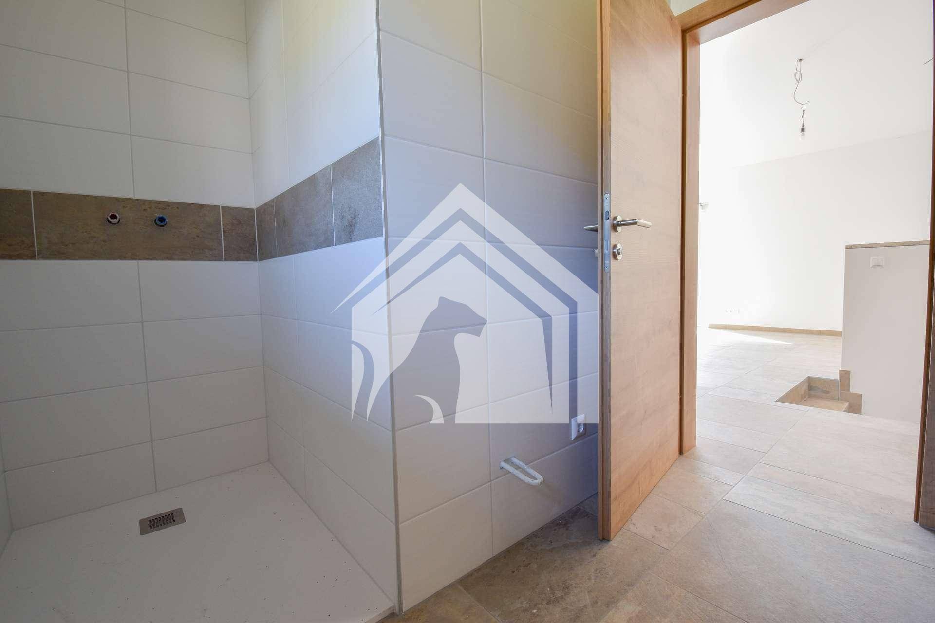 Badezimmer im Bau mit gefliester Duschkabine und vorbereiteten Anschlüssen für Armaturen.