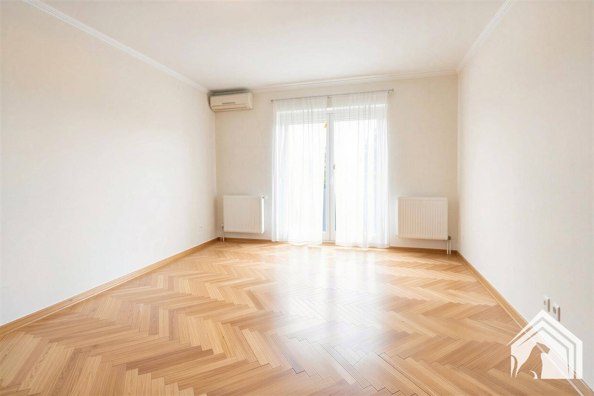 Leeres Wohnzimmer mit Fischgrätparkett, Klimaanlage und Zugang zum Balkon.