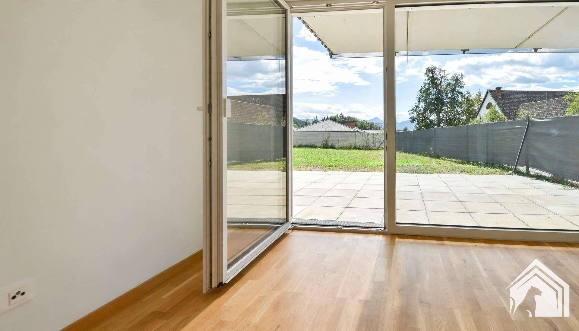 Heller Innenraum mit Blick auf die Terrasse und den Garten durch große Glasfenster.