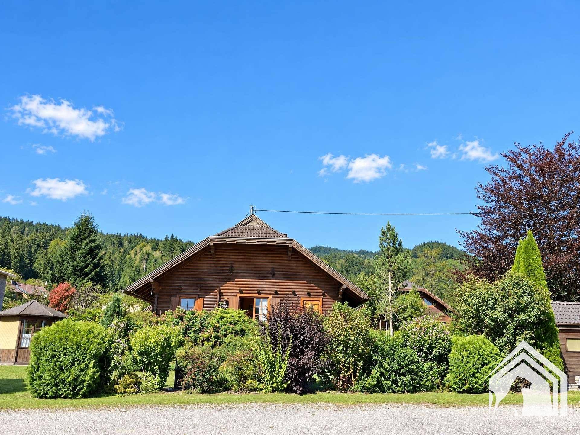 Charmantes Holzhaus umgeben von üppigem Grün und Bäumen unter blauem Himmel.