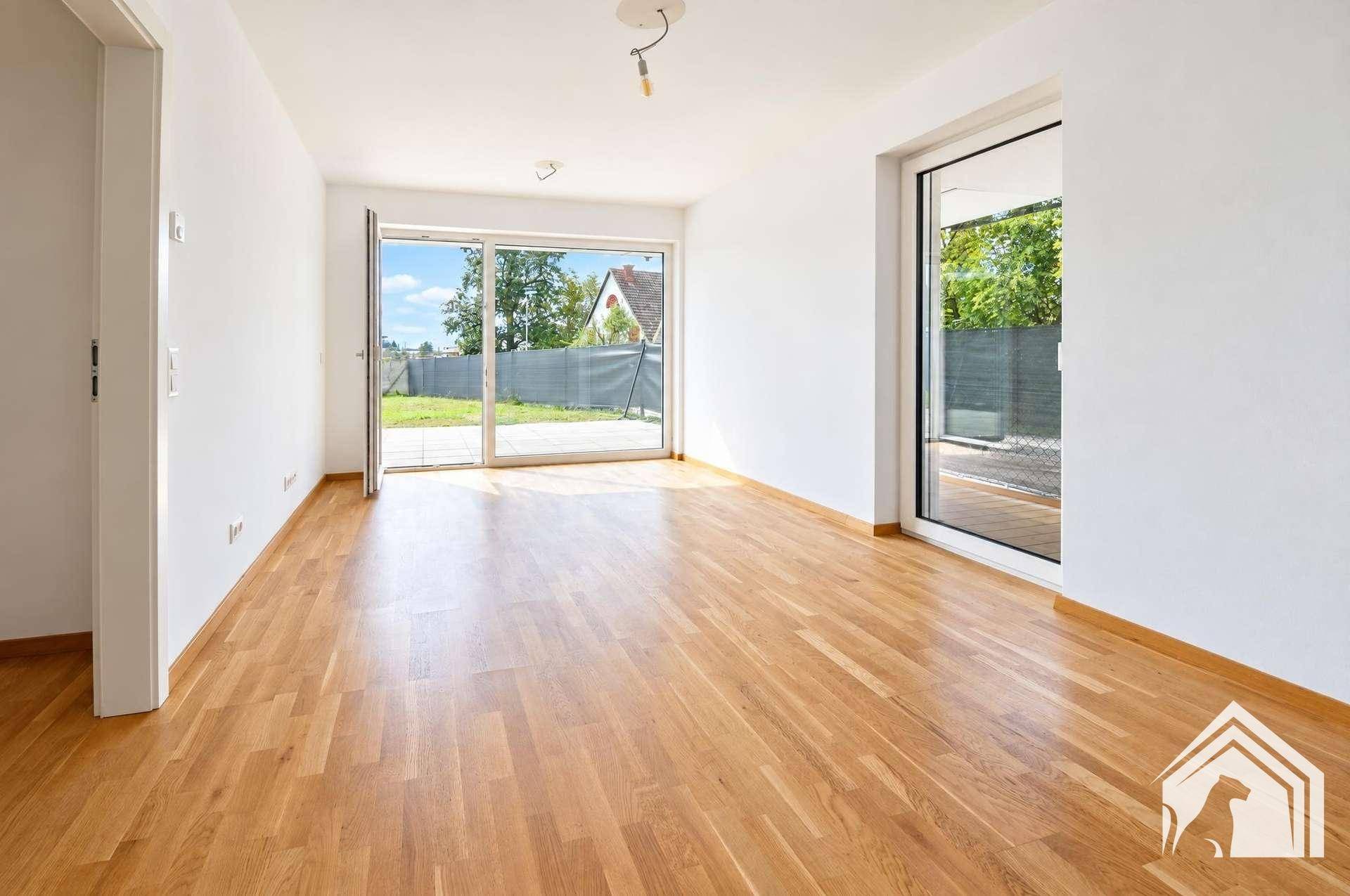 Heller Wohnbereich mit Holzboden und großen Fenstern, die viel Tageslicht hereinlassen.