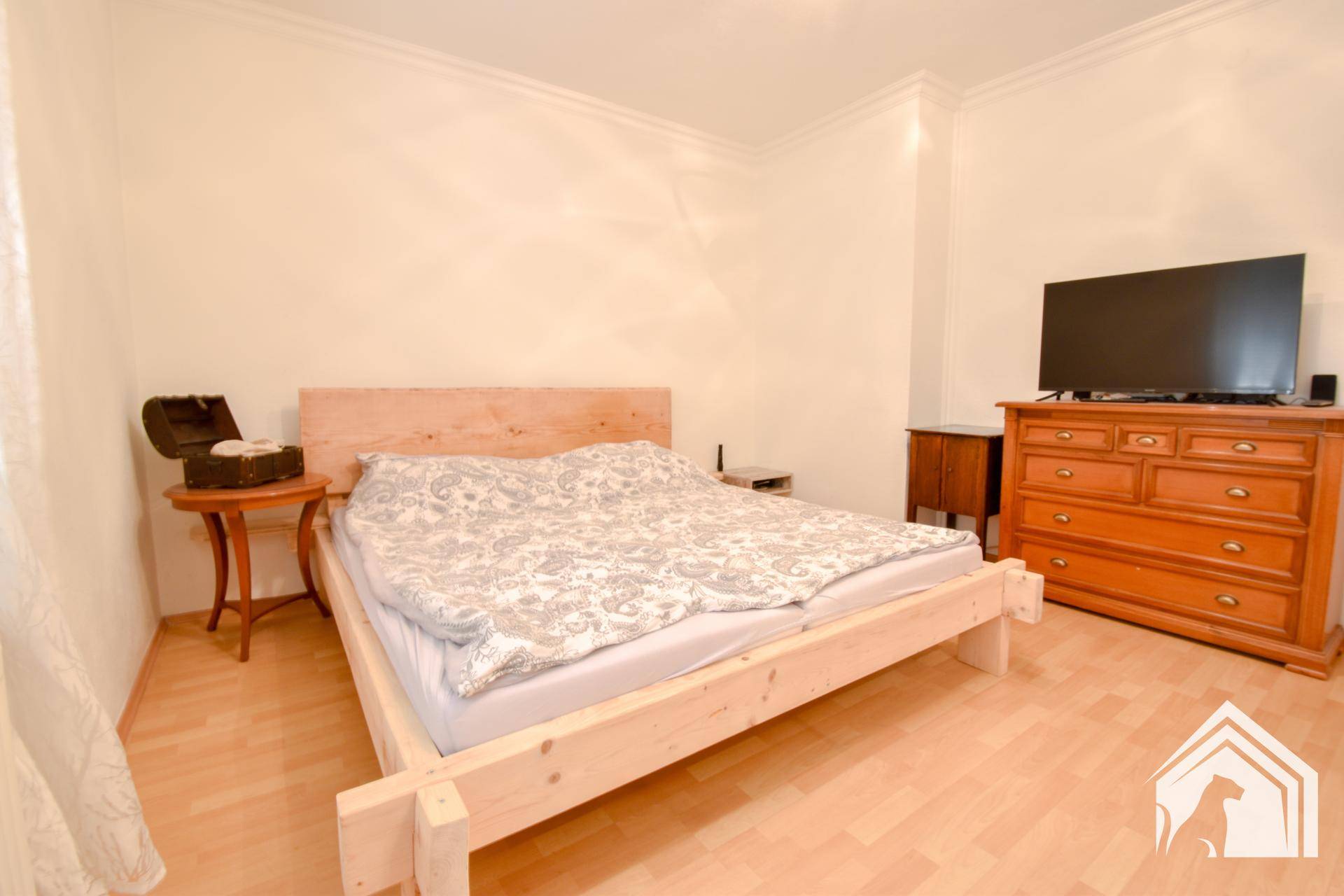 Schlafzimmer mit hellem Holzbett, Kommode und Laminatboden, bereit zur individuellen Gestaltung.