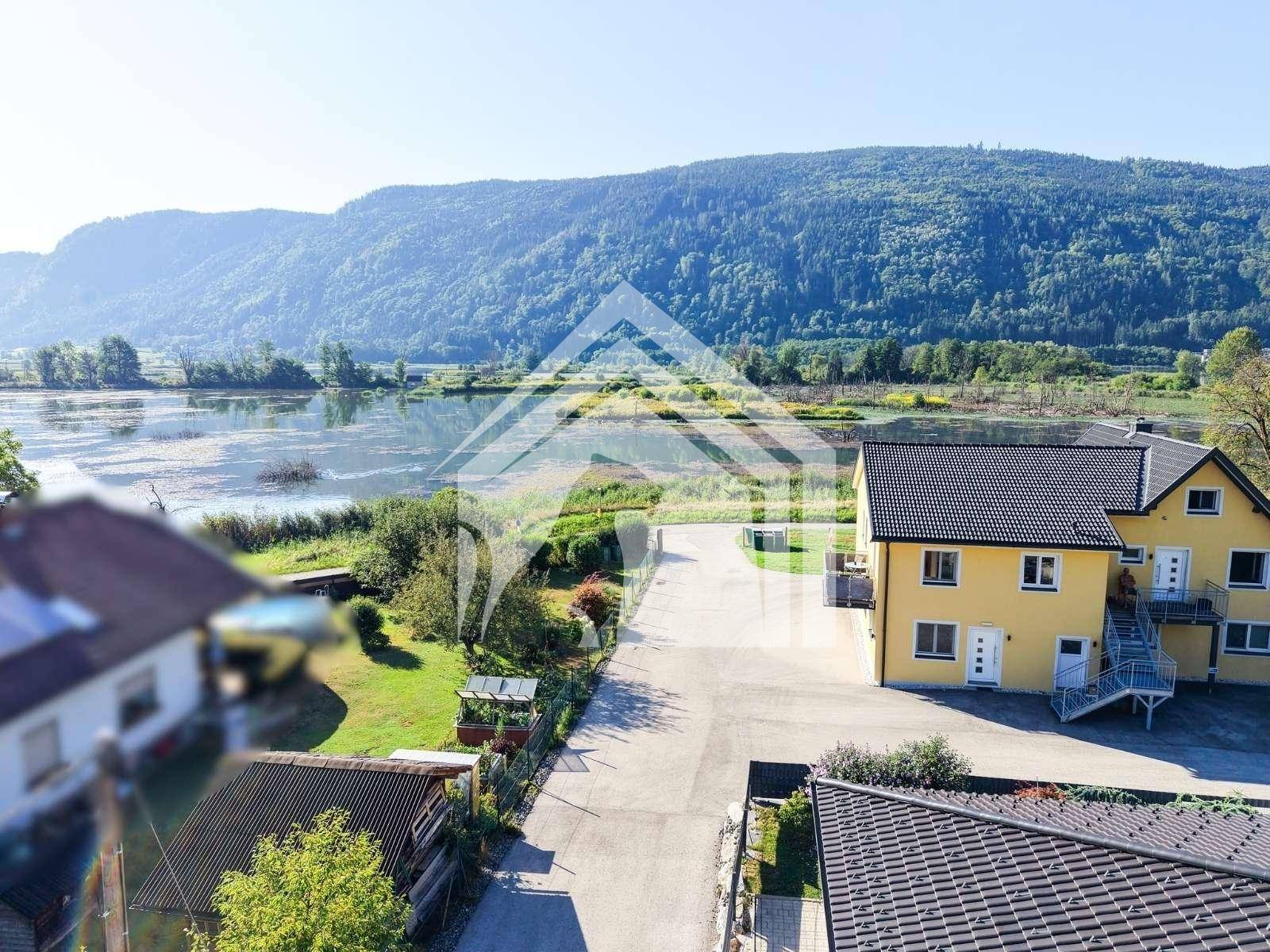 Luftaufnahme eines gelben Gebäudes am Seeufer mit Blick auf die umliegende Natur und Berge.