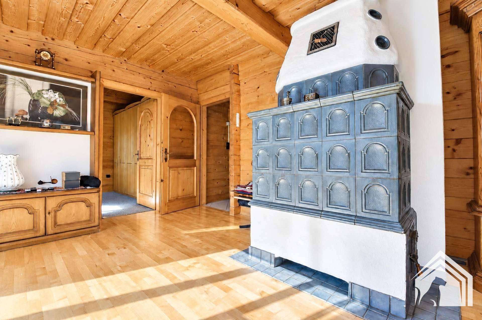 Geräumiges Wohnzimmer mit Holzboden, Holzbalkendecke und einem traditionellen Kachelofen.