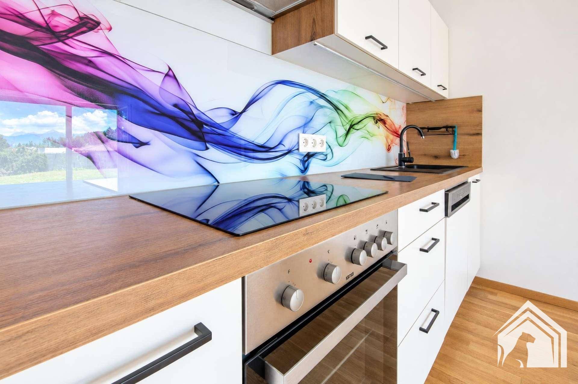 Detailansicht der modernen Küche mit Induktionskochfeld, Holzarbeitsplatte und farbigem Spritzschutz.
