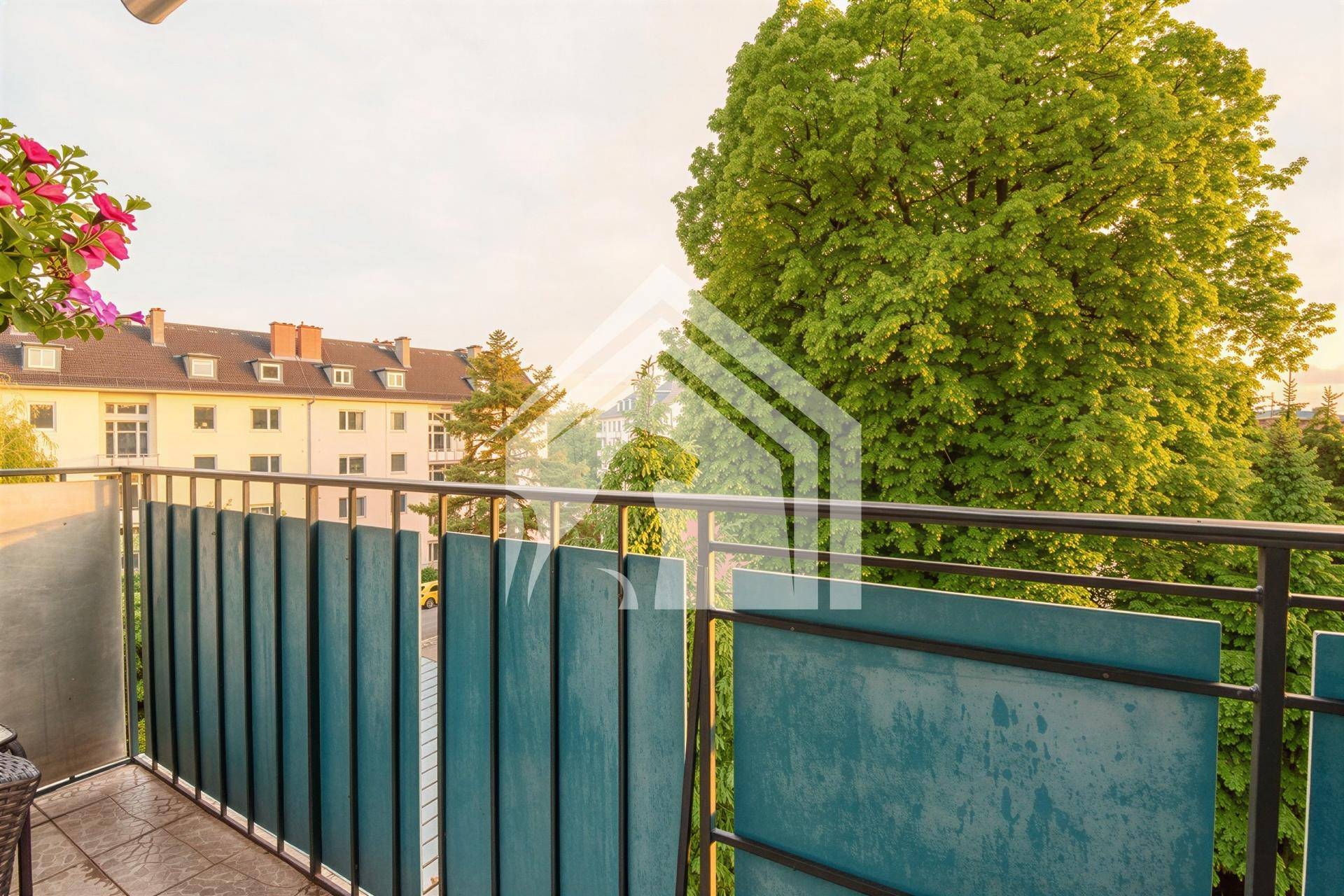 Balkon mit grünen Sichtschutzwänden und Blick auf Bäume und umliegende Gebäude.