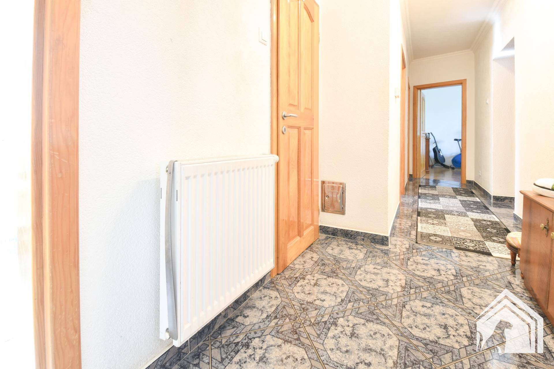 Flur mit gemusterten Fliesen, Holztüren und Heizkörper, der zu weiteren Räumen führt.