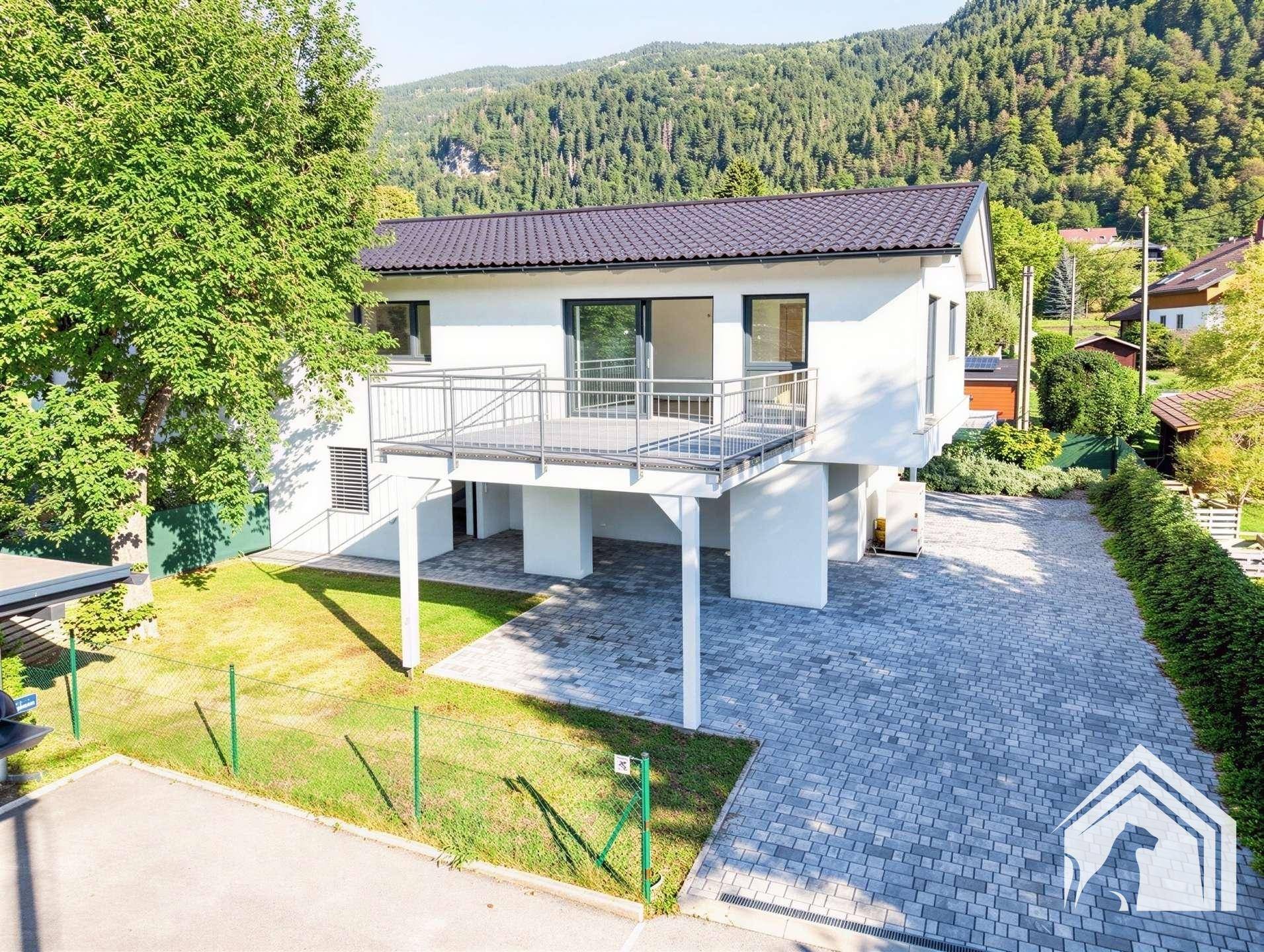 Vorderansicht des modernen Hauses mit großer Terrasse, gepflasterter Auffahrt und Bergblick.