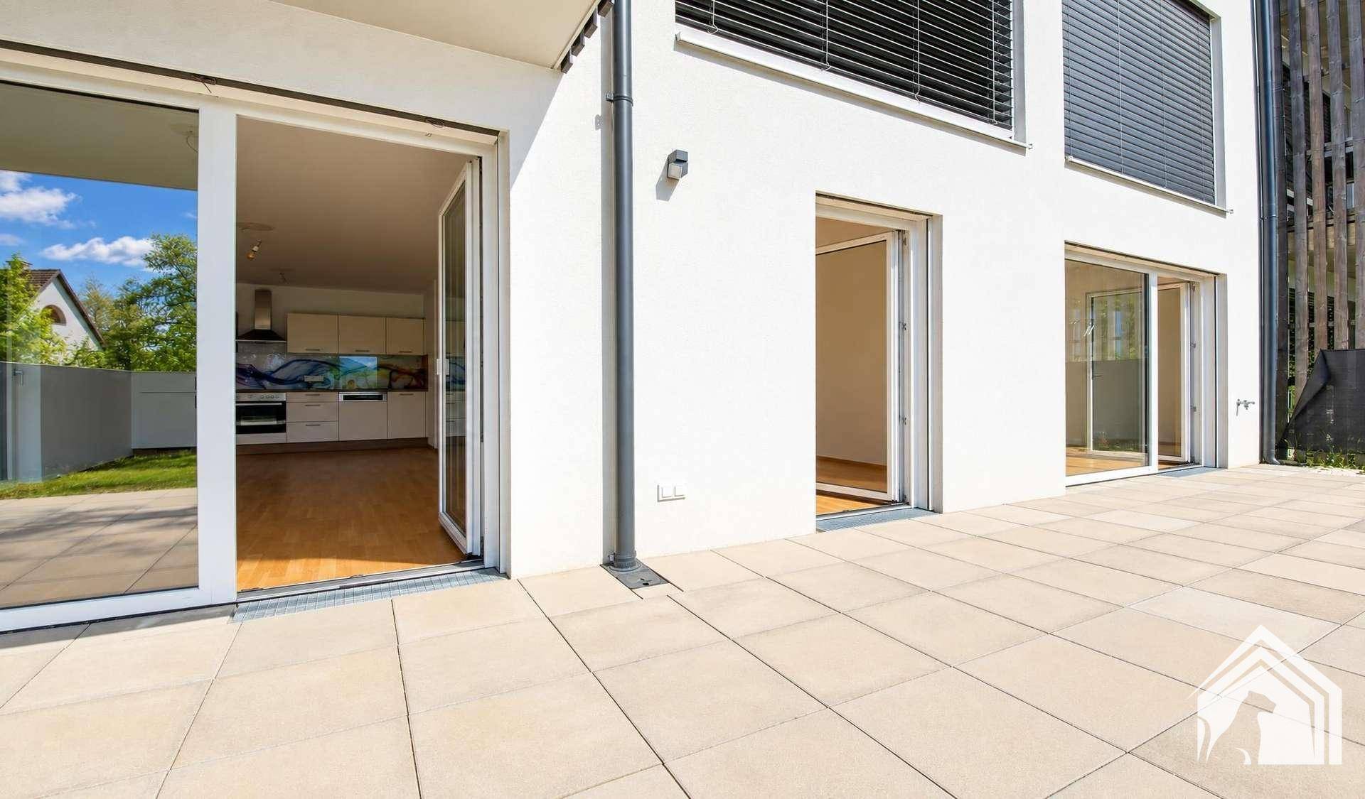 Große, helle Terrasse mit Zugang zu mehreren Räumen und Blick auf die moderne Fassade.