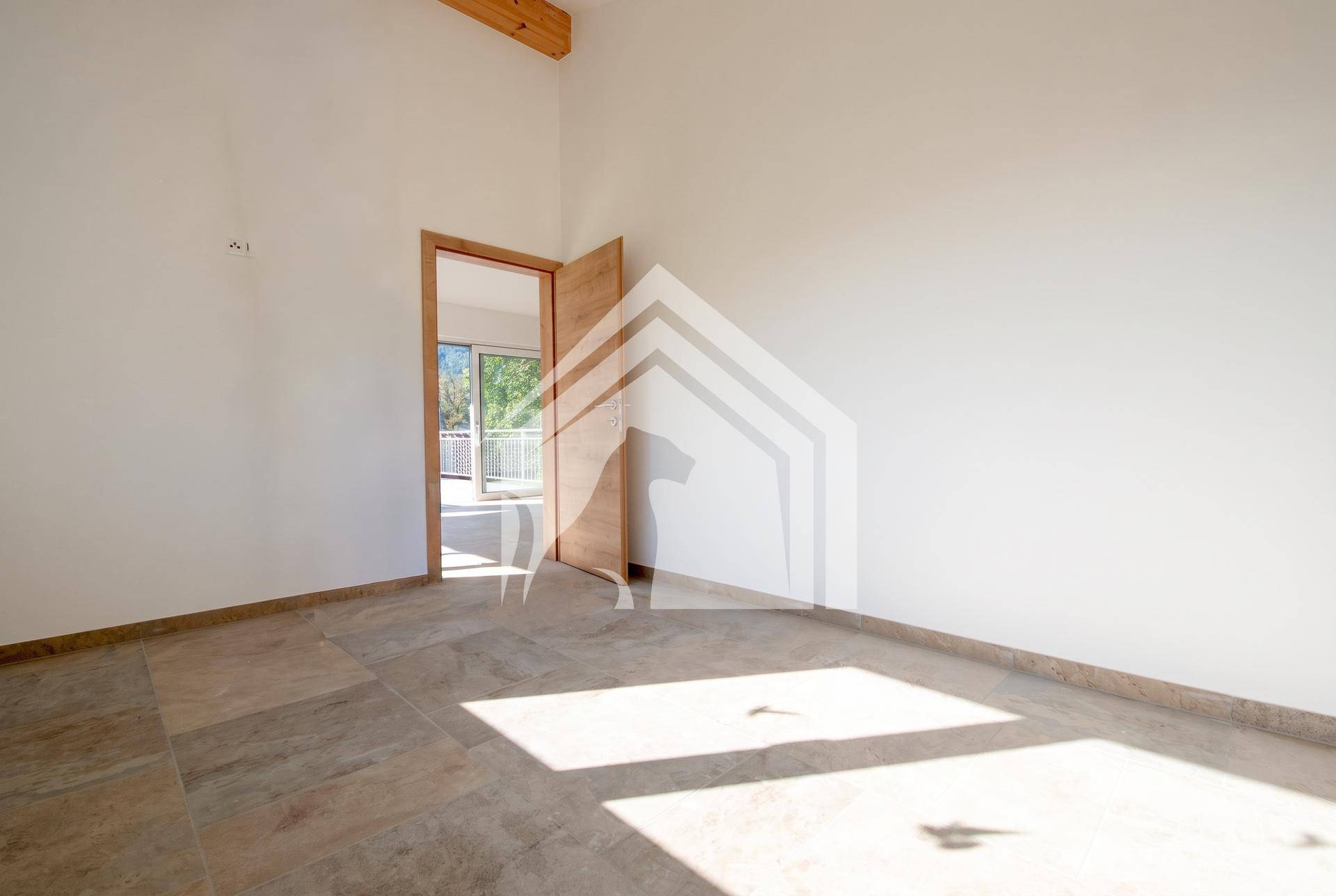 Helles, leeres Zimmer mit Fliesenboden, Holztür und viel natürlichem Licht.