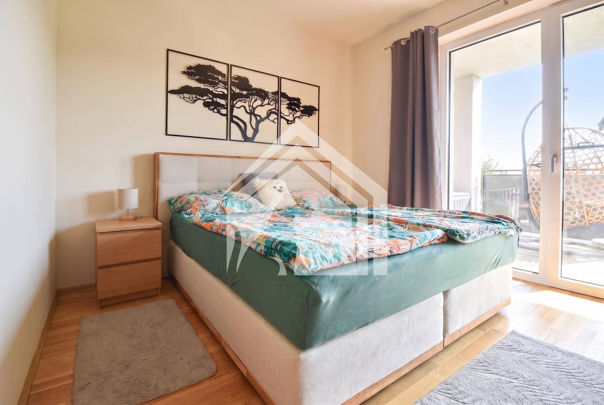 Gemütliches Schlafzimmer mit Holzboden, Doppelbett und Zugang zum sonnigen Balkon.