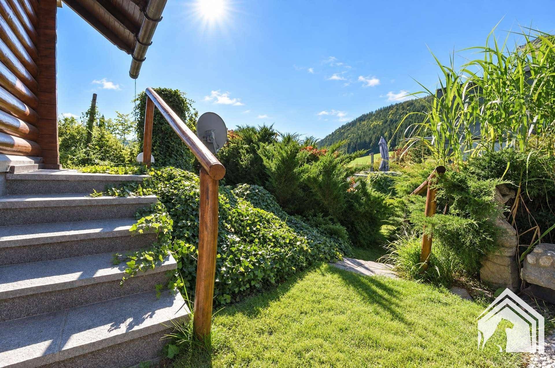 Steintreppe mit Holzgeländer, umgeben von grünen Sträuchern und Rasen.