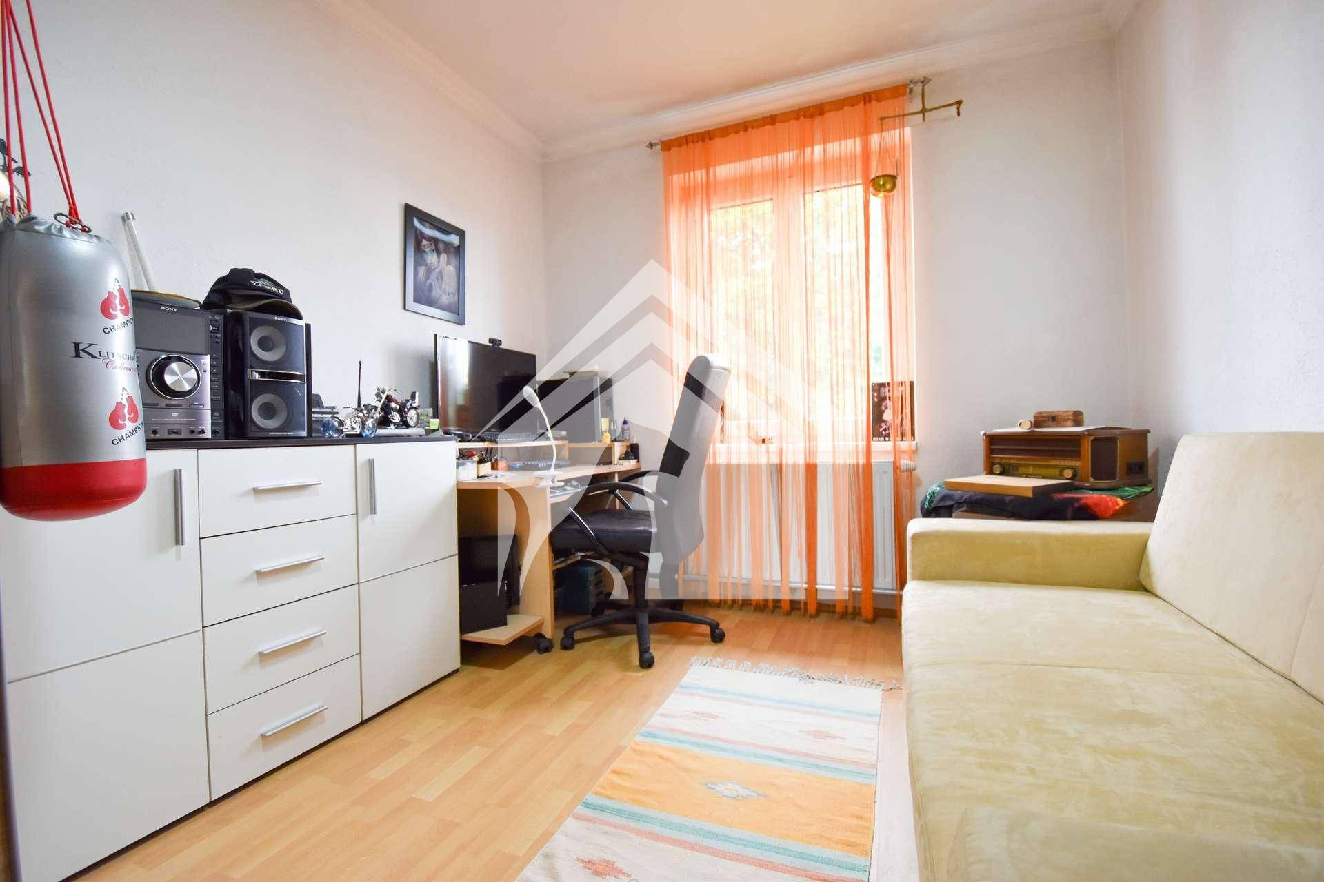 Helles Arbeitszimmer mit Schreibtisch, Schrank und einem kleinen Sofa.