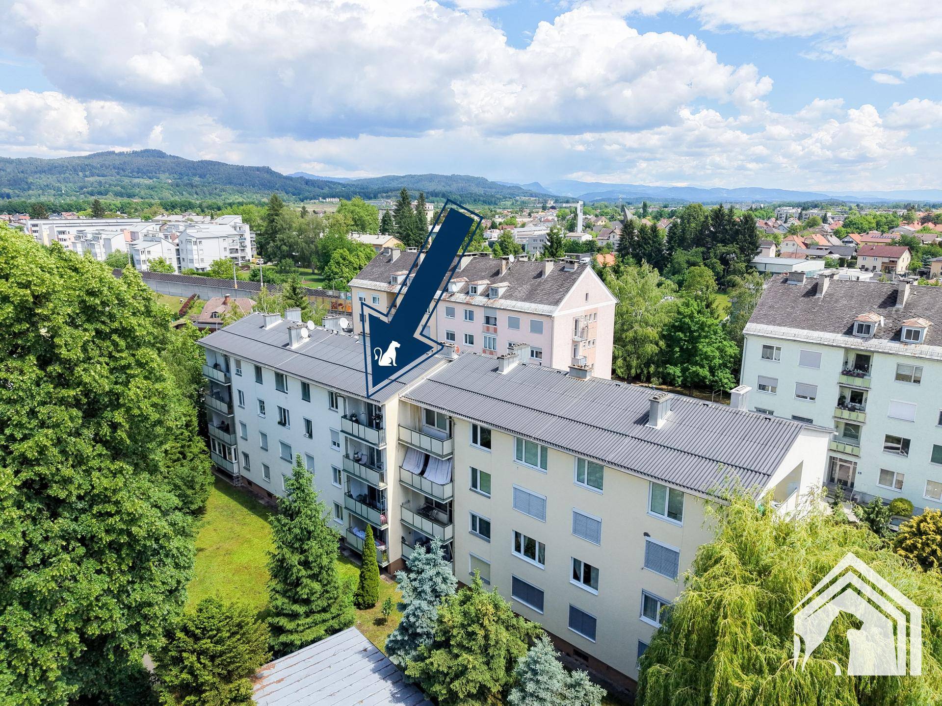 Luftaufnahme des Wohngebäudes mit umliegender Grünfläche und Bergblick im Hintergrund.