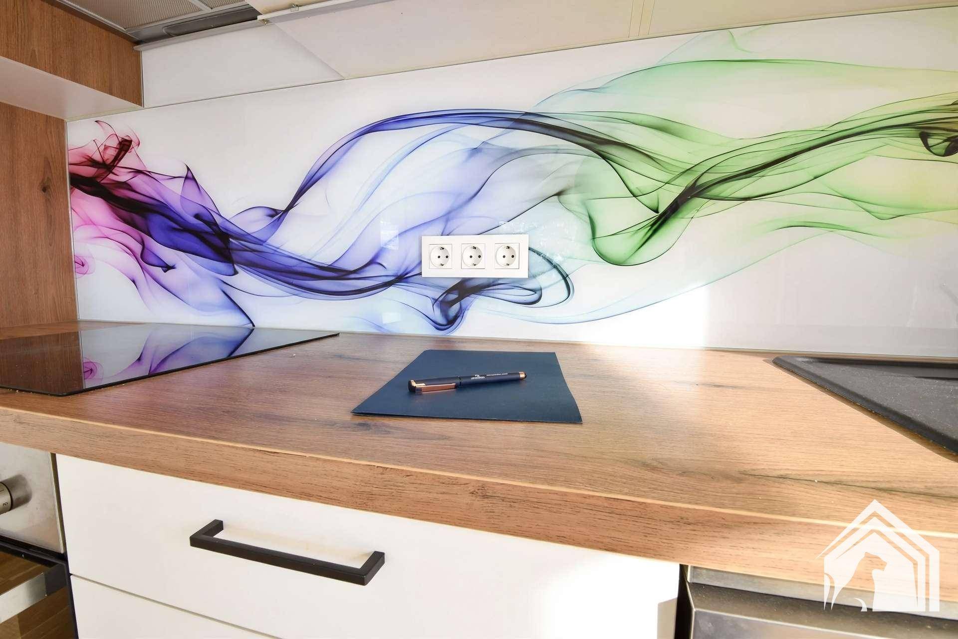 Nahaufnahme der Küchenarbeitsplatte aus Holz mit Steckdosen und farbenfrohem Glas-Spritzschutz.