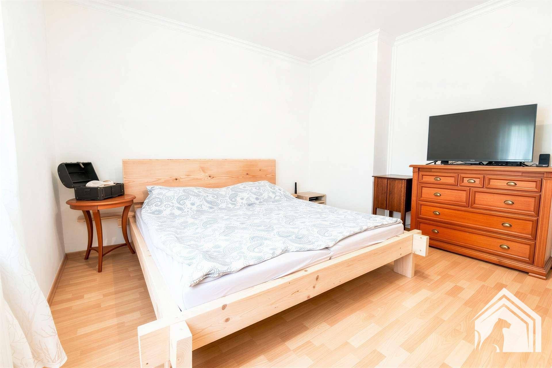 Schlafzimmer mit hellem Holzbett, Kommode und Laminatboden, bereit zur individuellen Gestaltung.
