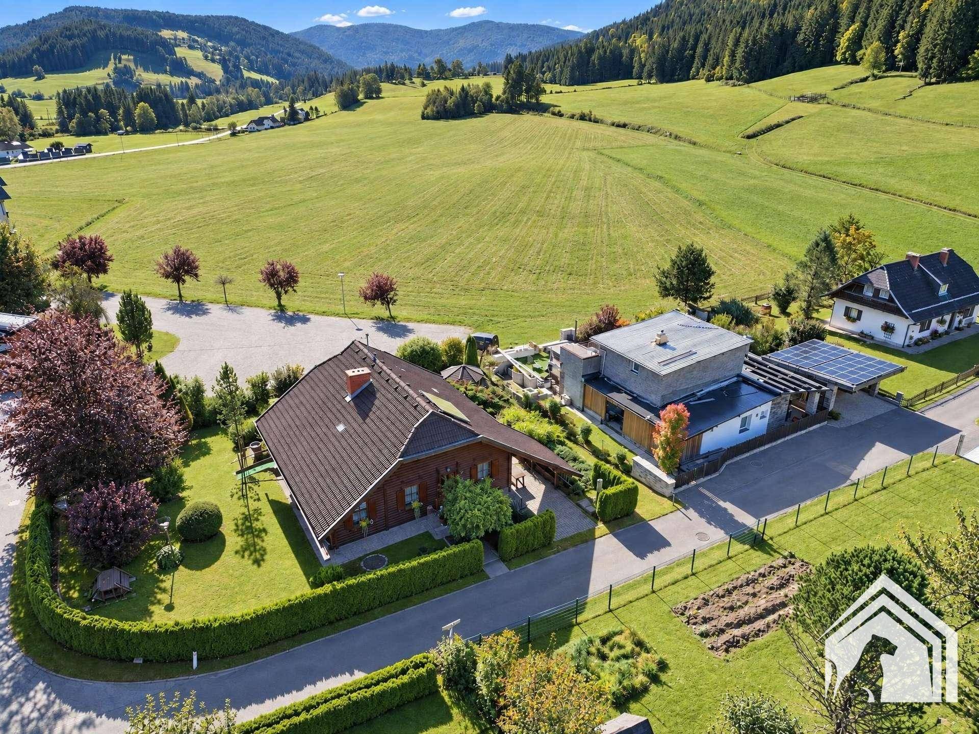 Weitläufige Luftaufnahme des Anwesens, eingebettet in grüne Wiesen und bewaldete Hügel.