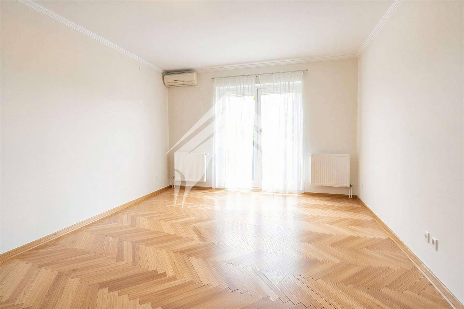 Heller, leerer Raum mit Fischgrätparkett, weißen Wänden und Zugang zu einem Balkon.