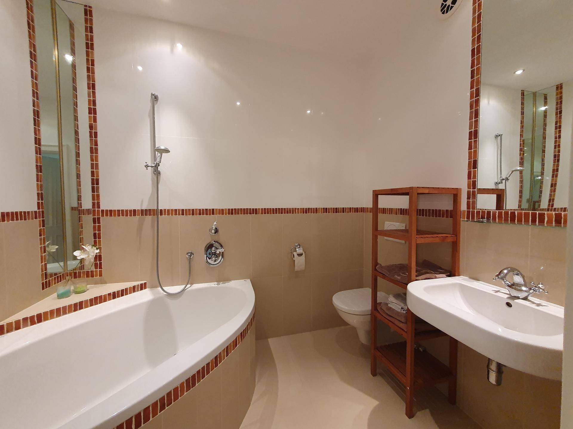 Badezimmer mit Eckbadewanne, Einzelwaschbecken und beigefarbenen Fliesen mit dekorativen Bordüren.