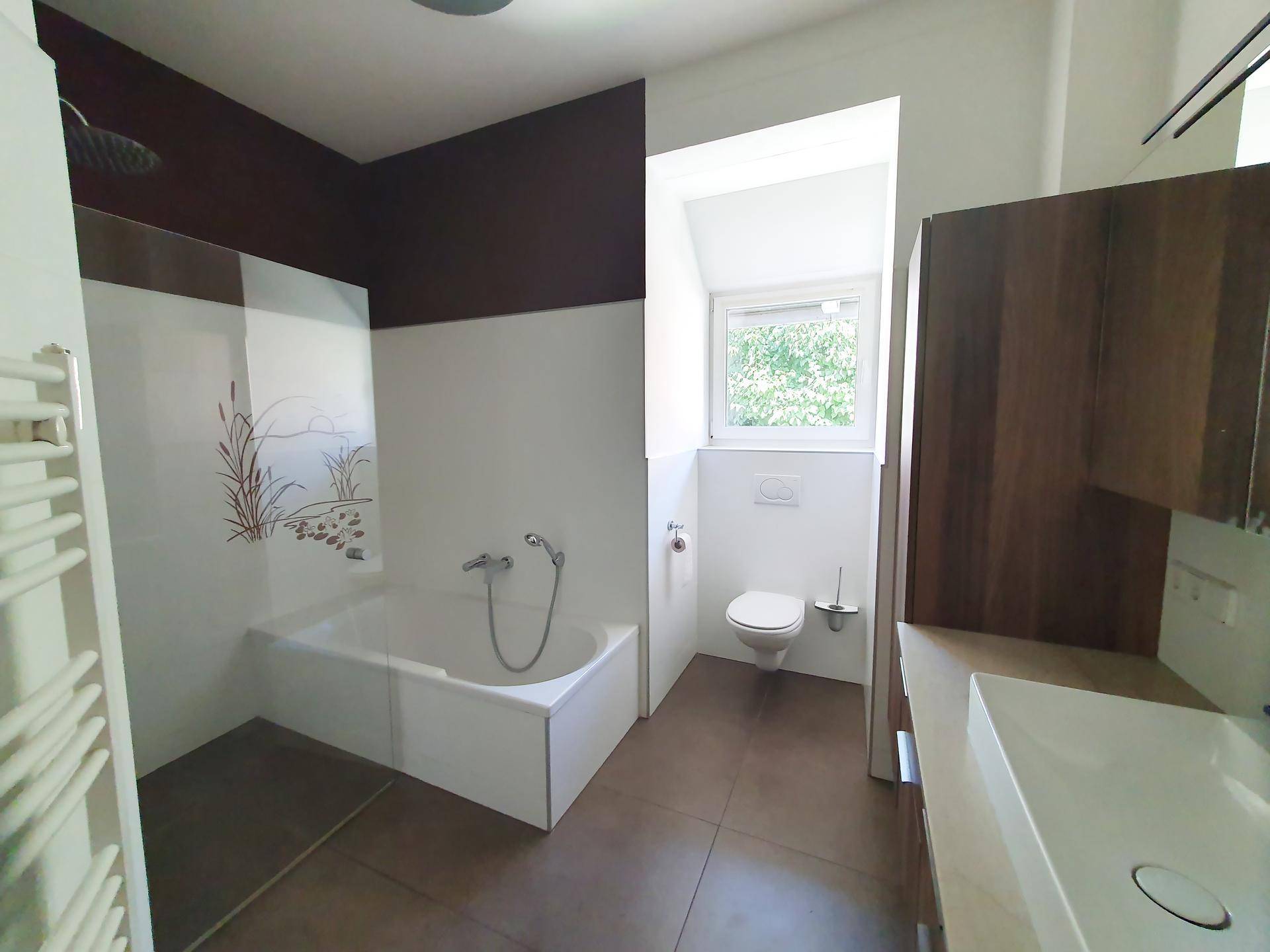 Modernes Badezimmer mit Badewanne, Dusche, WC und Fenster für Tageslicht.