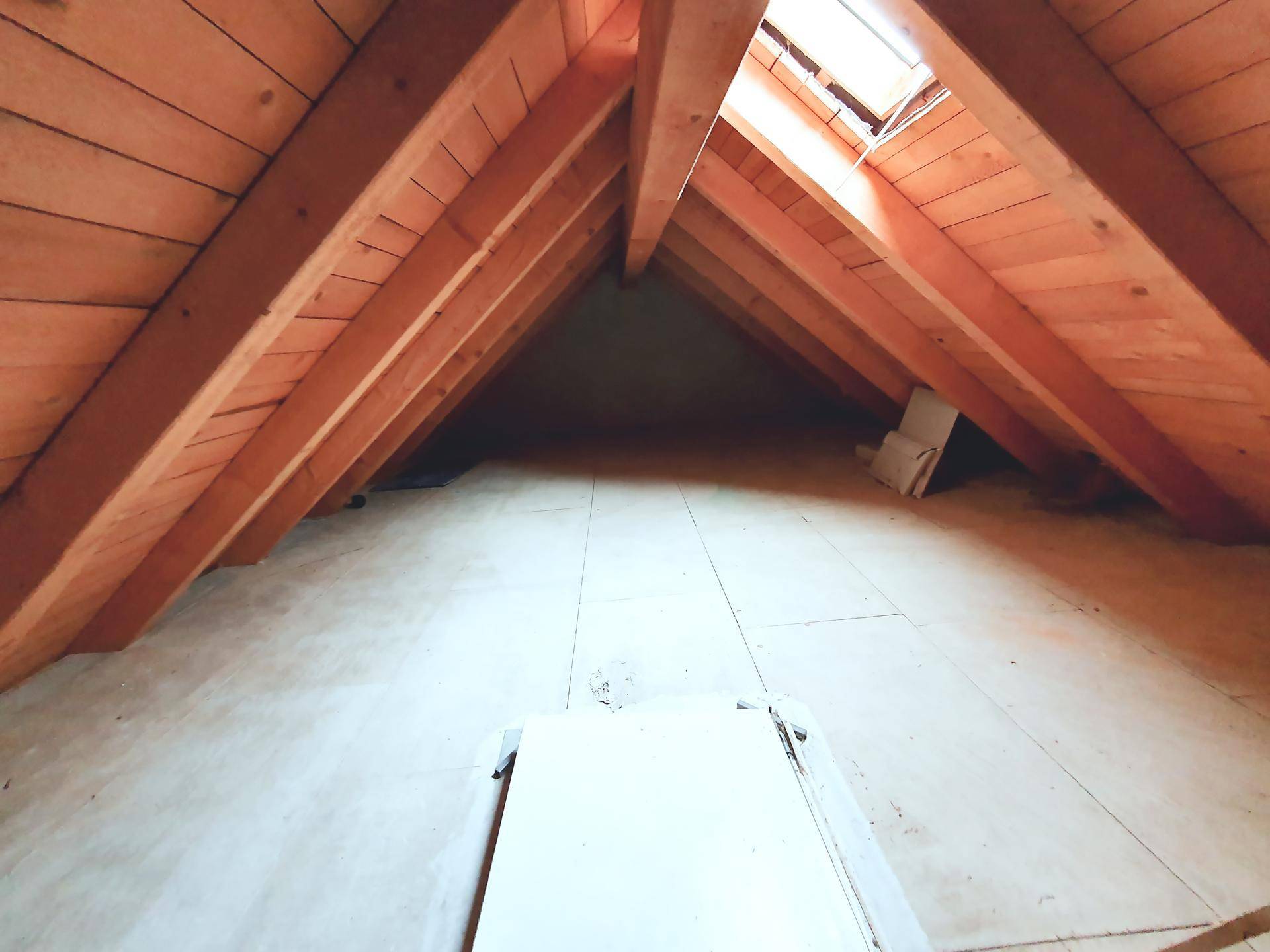 Geräumiger Dachboden mit sichtbaren Holzbalken und Dachfenster für natürliches Licht.