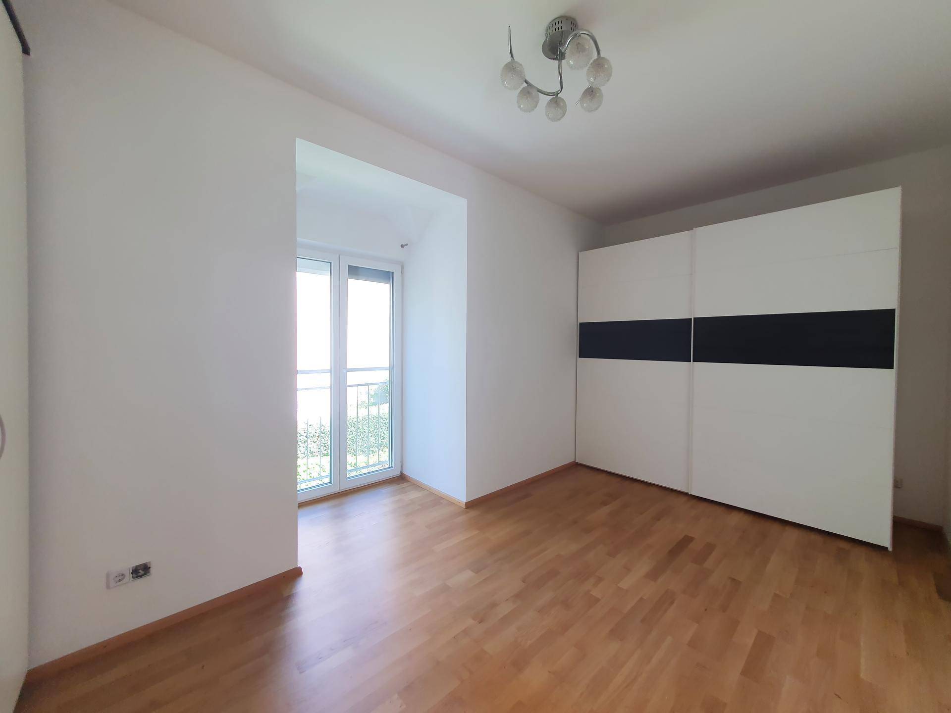 Schlafzimmer mit Holzboden, großem Kleiderschrank und Zugang zu einem französischen Balkon.