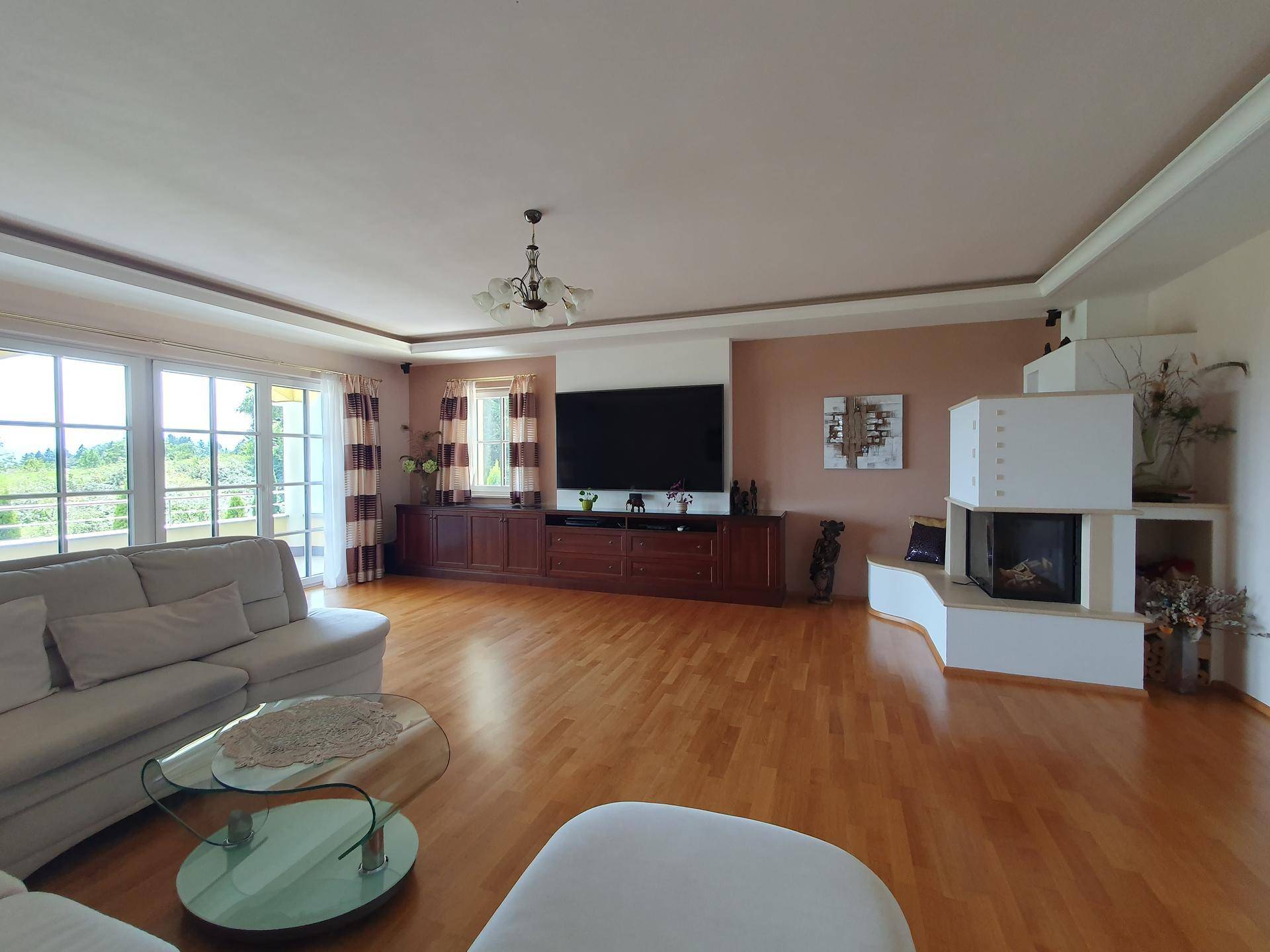 Helles Wohnzimmer mit Parkettboden, großem Kachelofen und Zugang zu einer Terrasse mit Weitblick.
