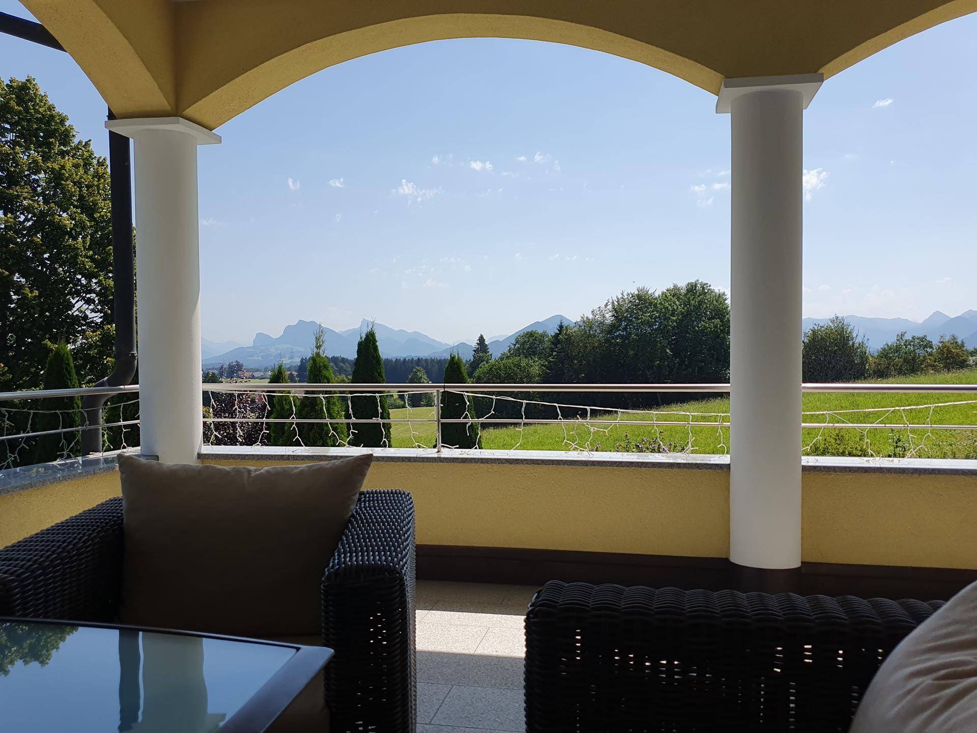 Überdachter Balkon mit bequemen Outdoor-Möbeln und einem weiten Blick auf die umliegende Landschaft und Berge.