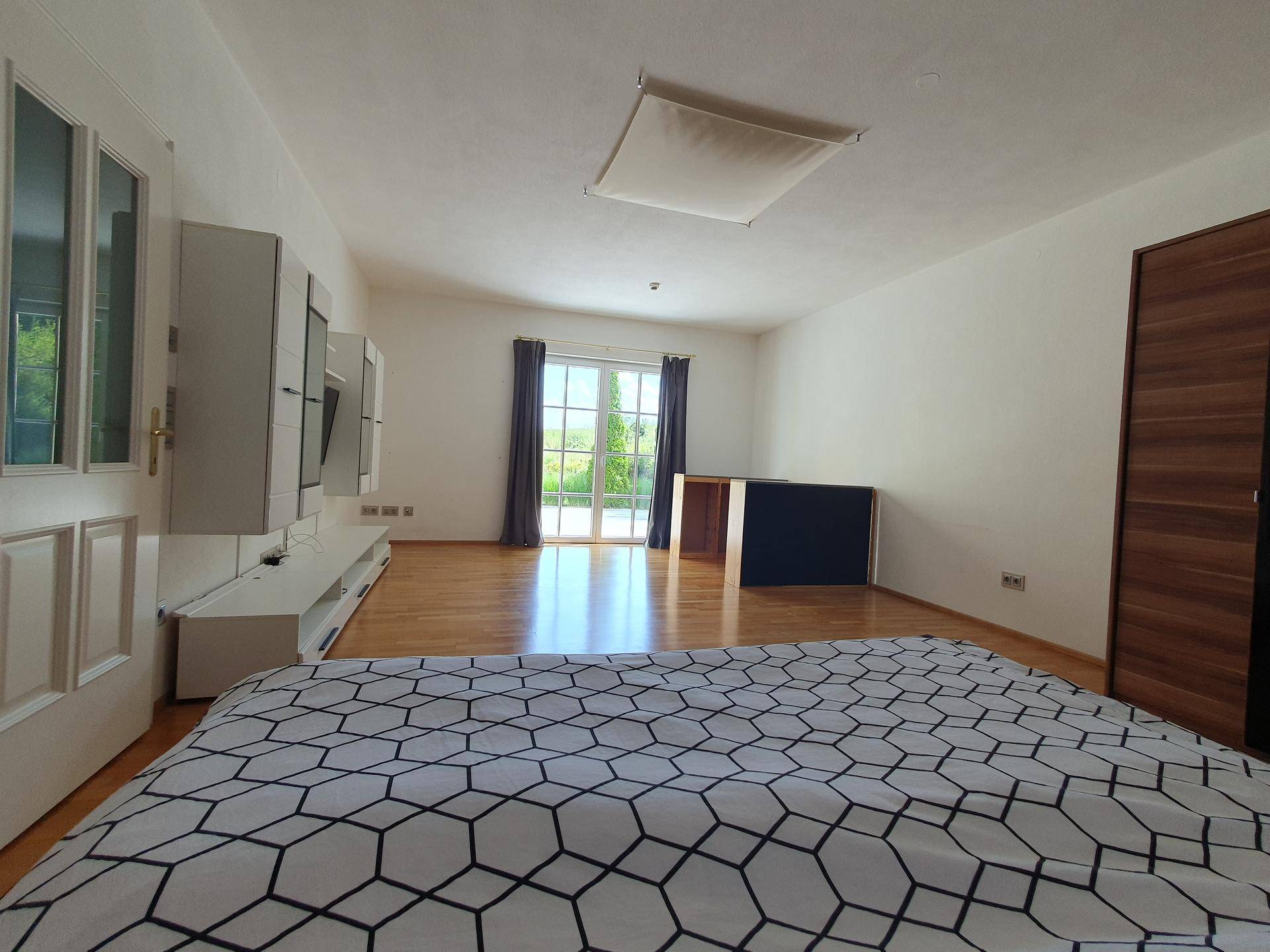 Geräumiges Schlafzimmer mit Holzboden, großen Fenstern und Zugang zu einem Außenbereich.