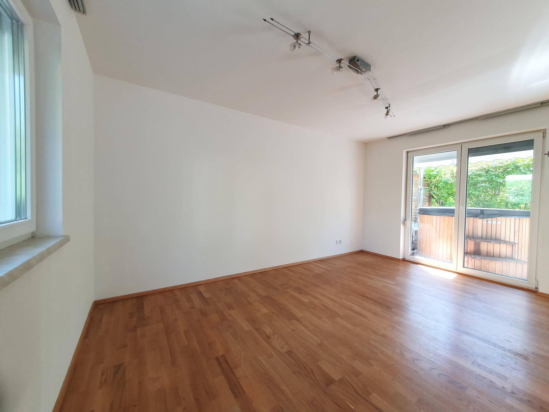 Geräumiges Wohnzimmer mit hellem Holzboden und großen Schiebetüren zum Außenbereich.