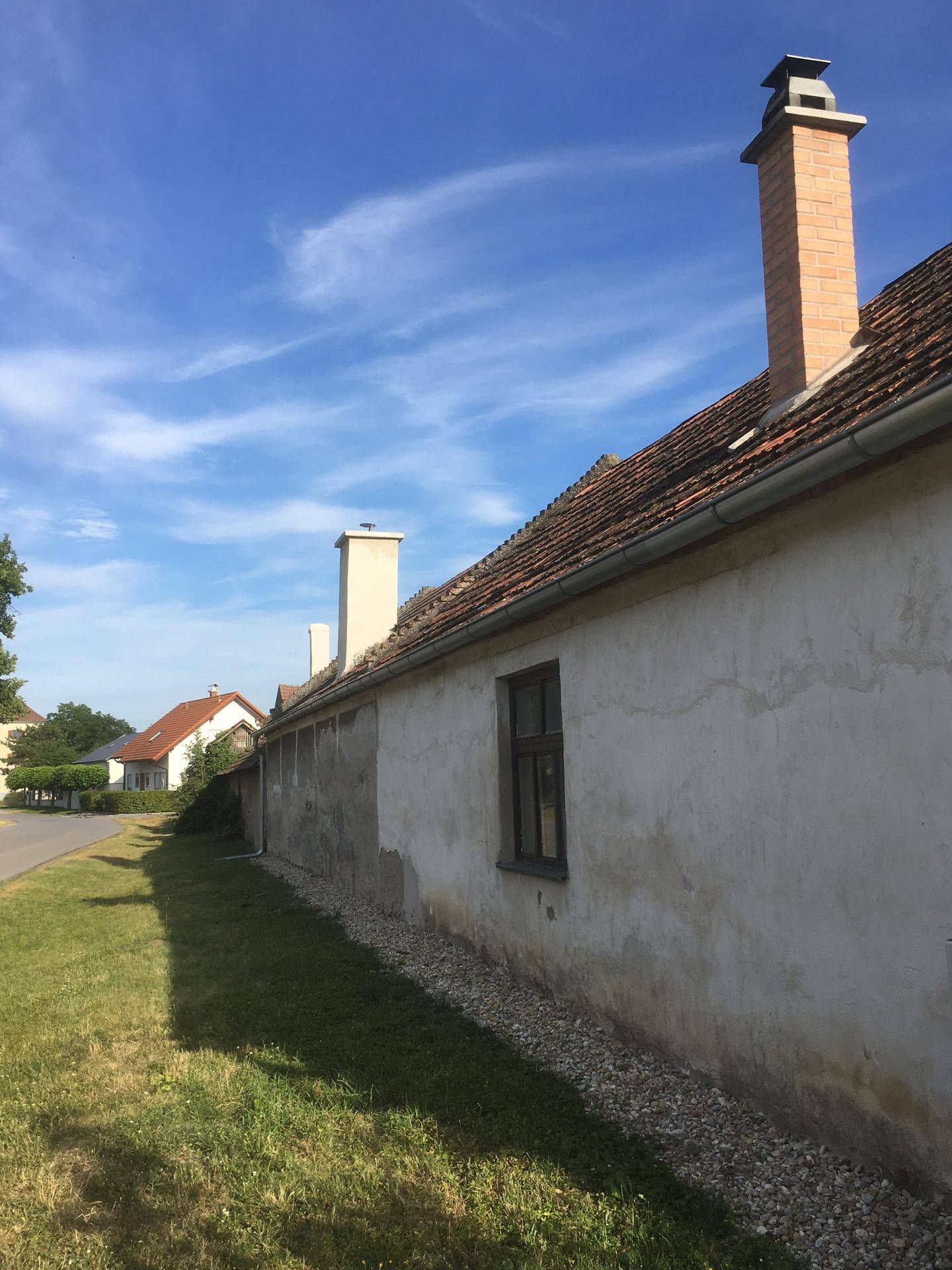 Lange Seitenfassade eines alten Gebäudes mit mehreren Schornsteinen und einem Ziegeldach.