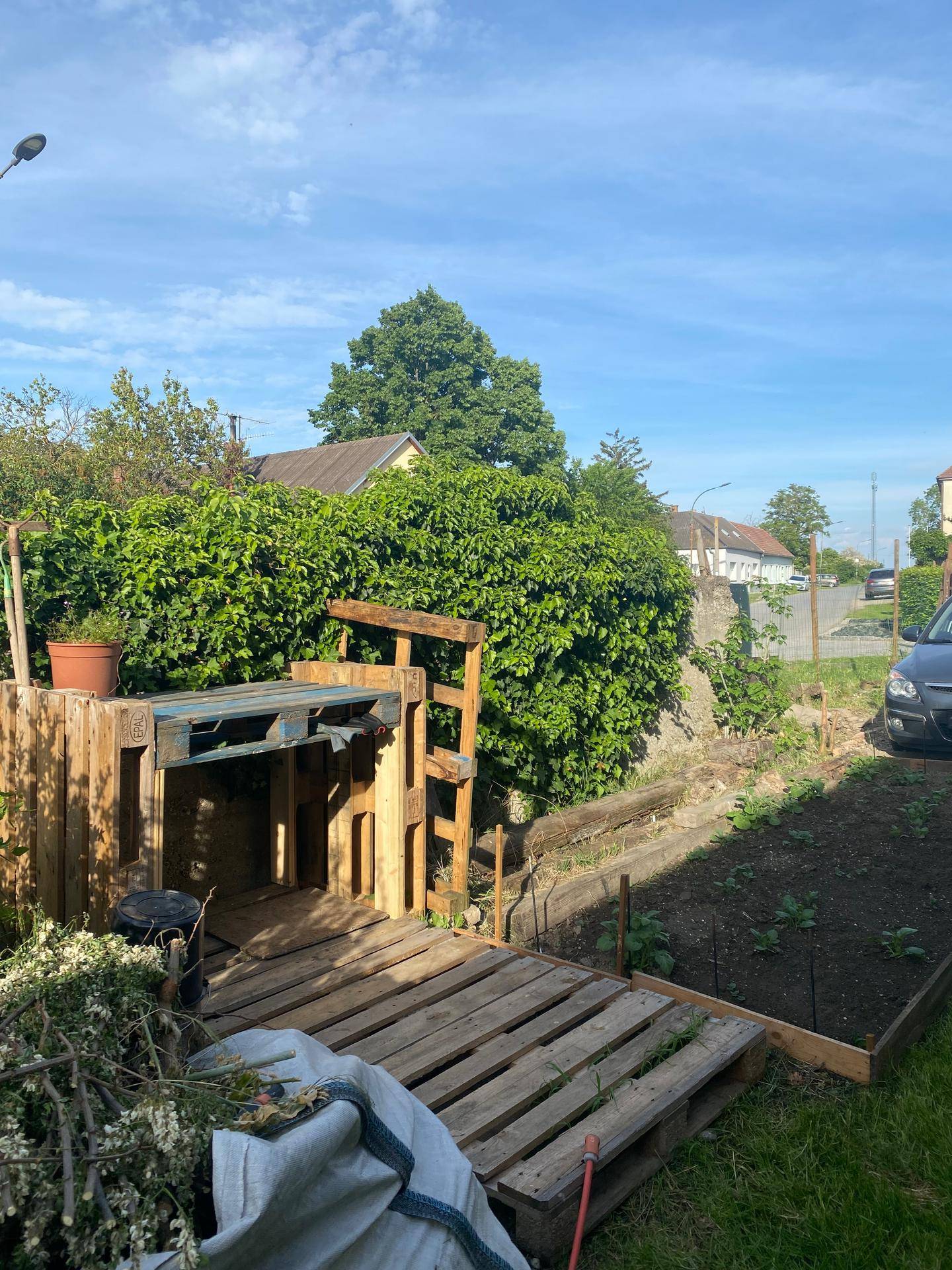 Gartenbereich mit Komposthaufen und einer dichten Hecke im Hintergrund.