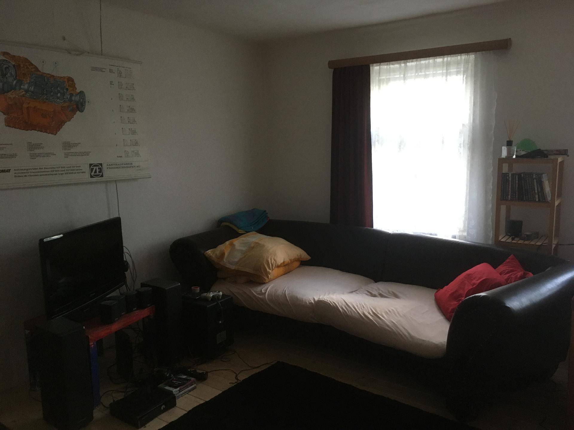 Wohnbereich mit dunklem Sofa, Fenster und Fernseher.