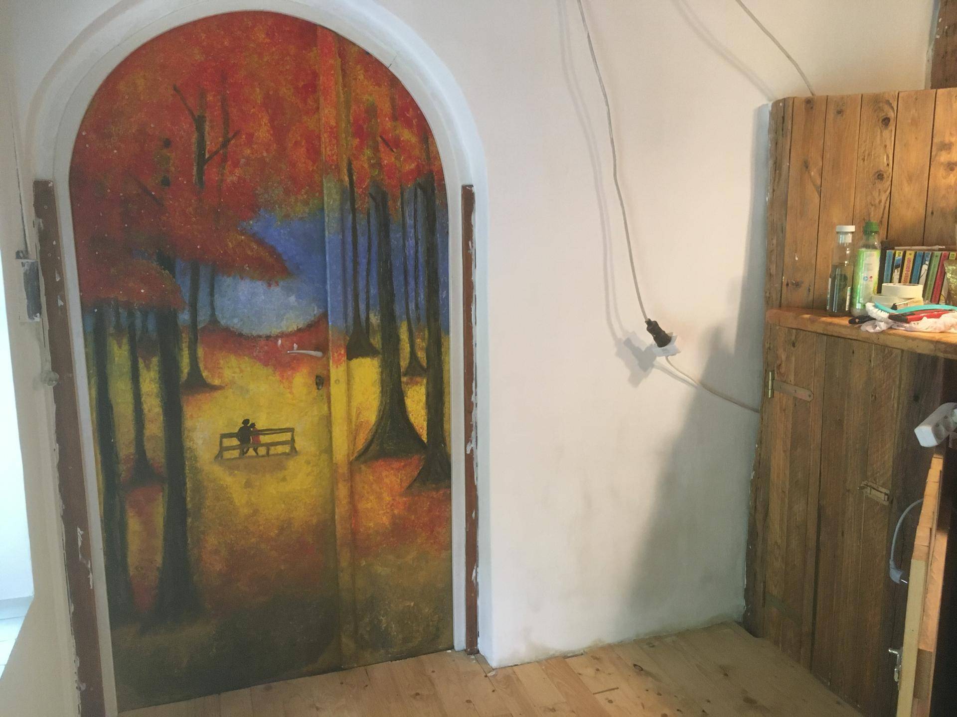Farbenfroh bemalte Tür mit Herbstmotiv in einem gewölbten Durchgang und Holzboden.