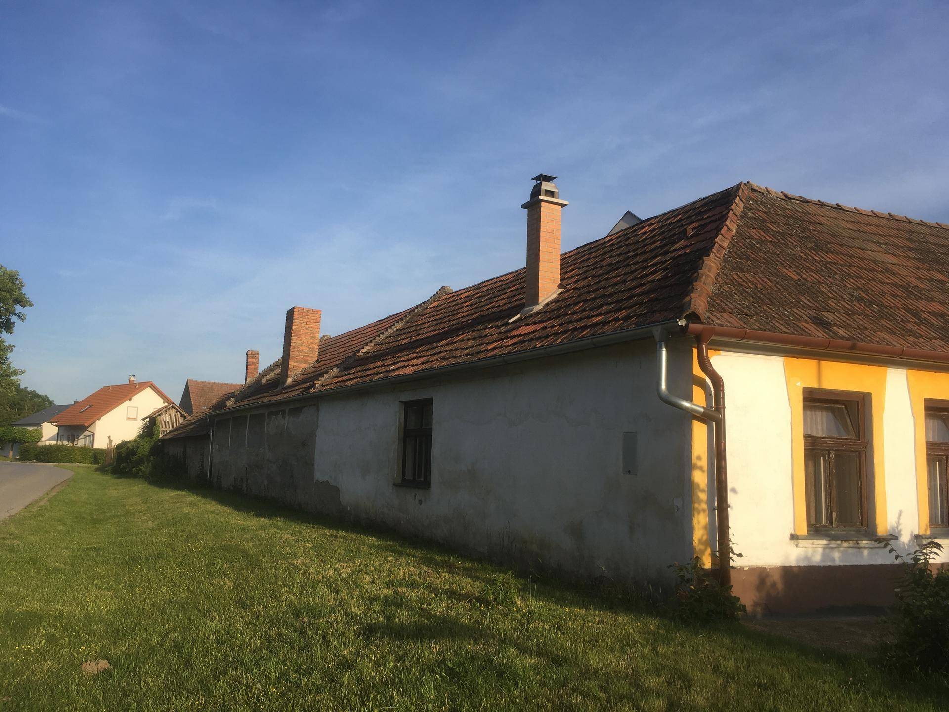 Seitenansicht eines alten Landhauses mit langen Mauern, Schornsteinen und rotem Ziegeldach.