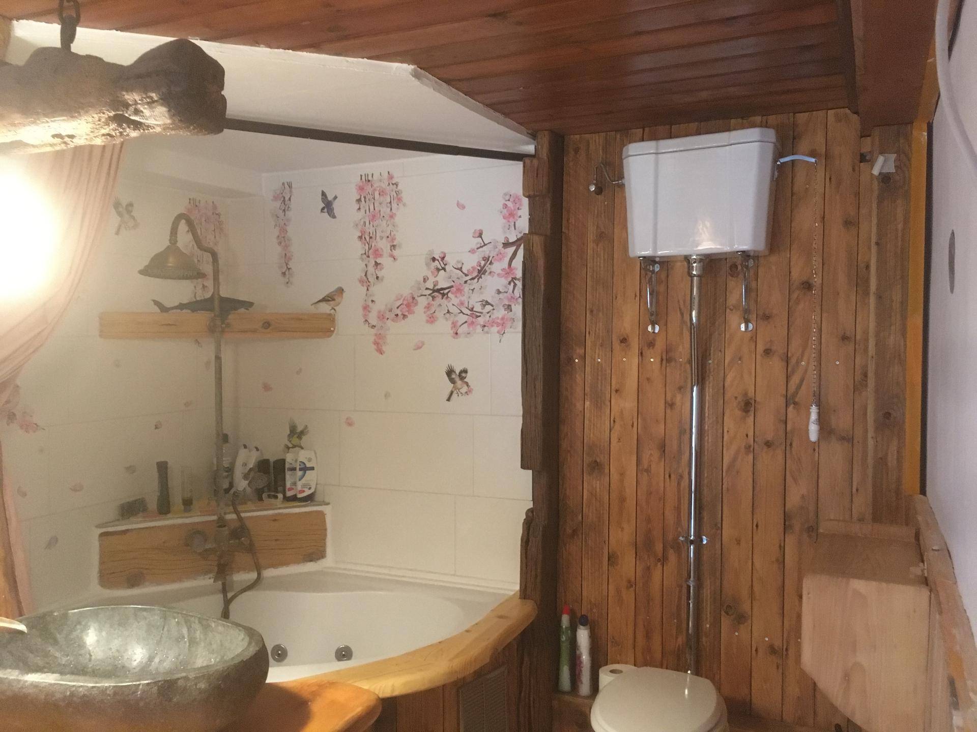 Badezimmer mit Eckbadewanne, Holzverkleidung und hoher Toilette.