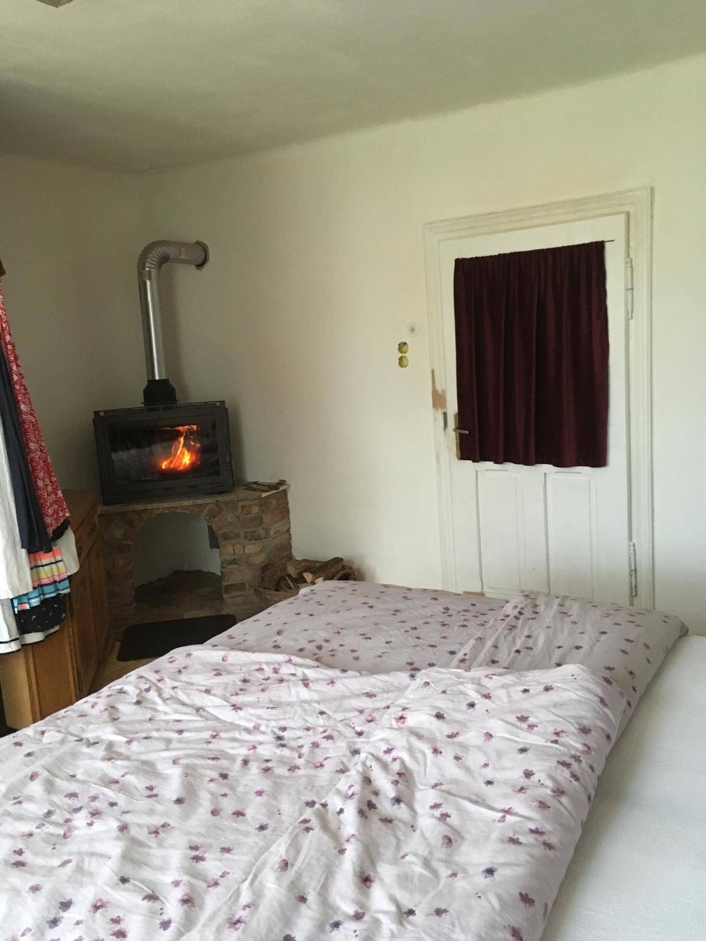 Schlafzimmer mit Kaminofen, Holzboden und floraler Bettwäsche.