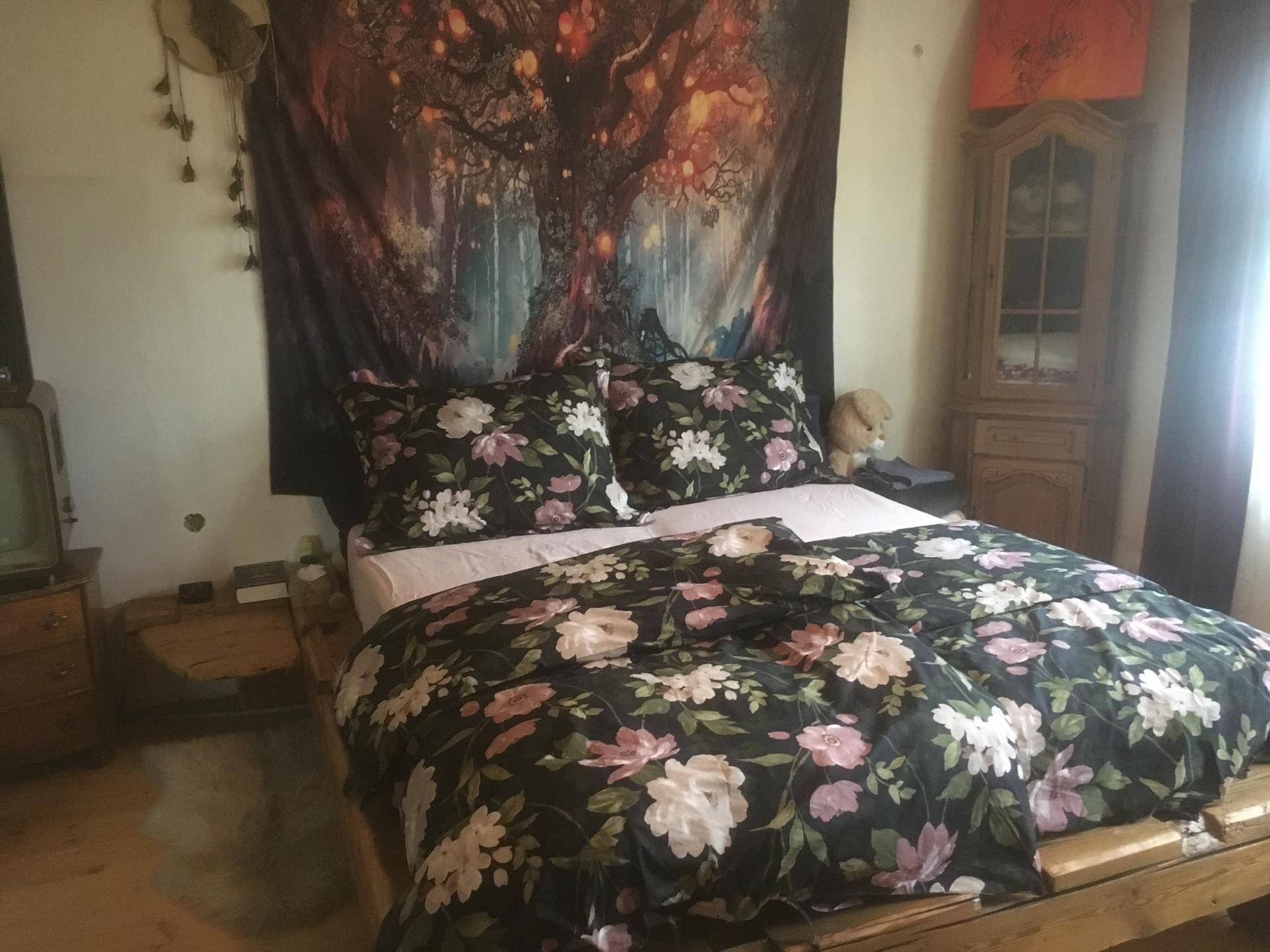 Schlafzimmer mit großem Bett, floraler Bettwäsche und einem dekorativen Wandteppich.