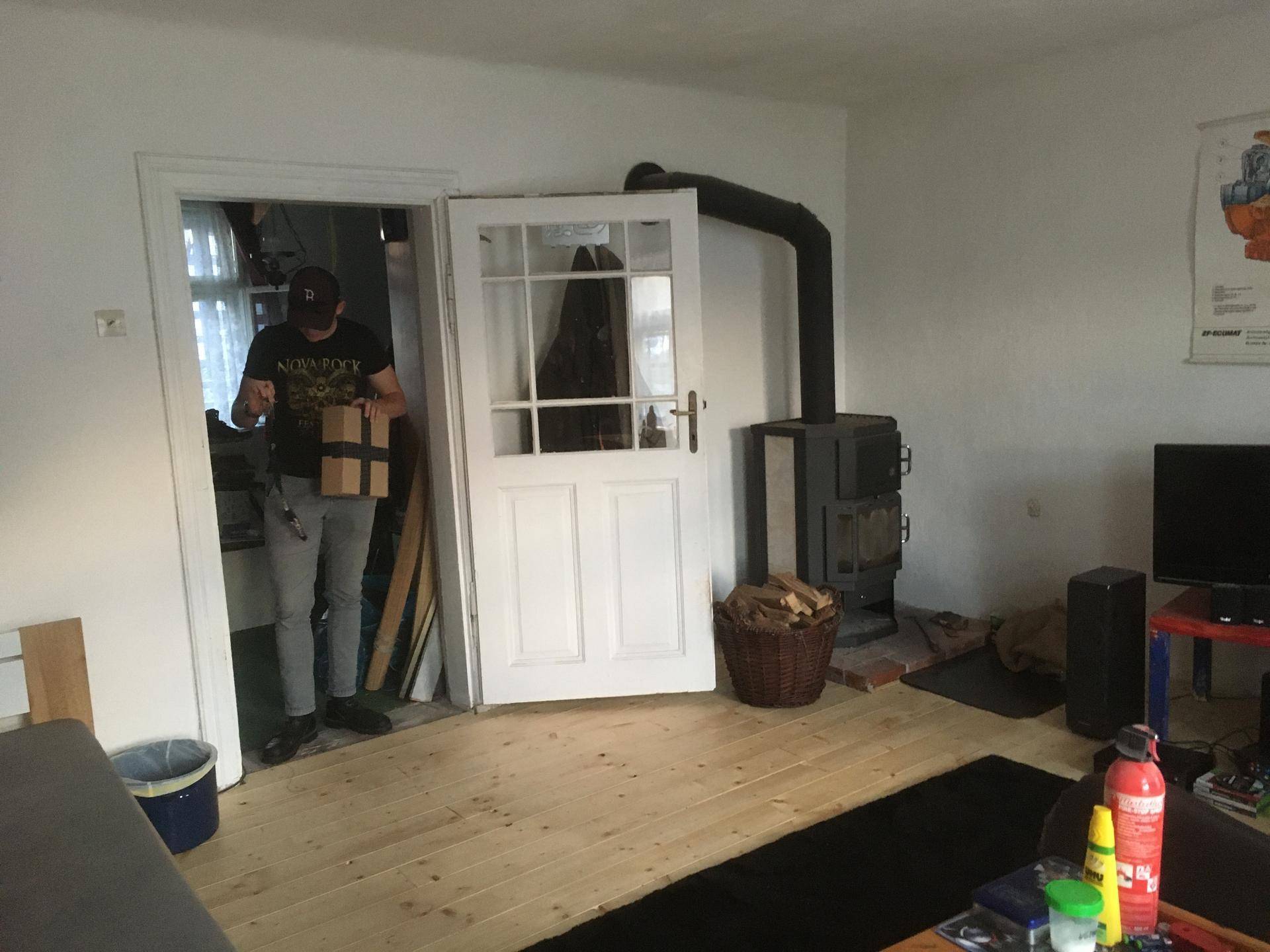 Wohnzimmer mit Kaminofen, Holzboden und Zugang zu einem weiteren Raum.