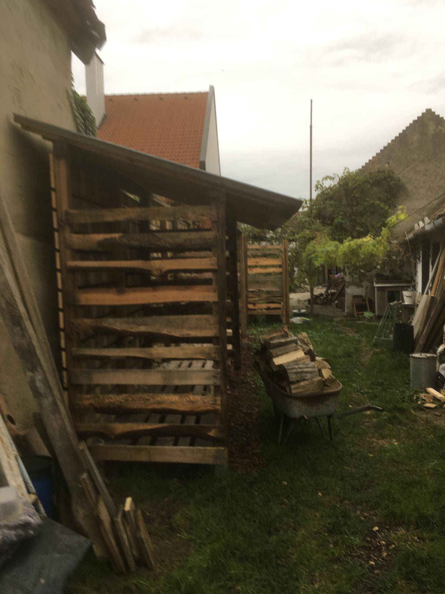 Holzunterstand im Garten mit gestapeltem Brennholz, rustikaler Charme.